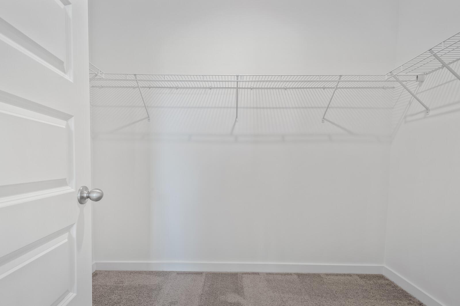 Spacious walk-in master closet in The Asheville home with wire shelving, white walls, and carpeted floor