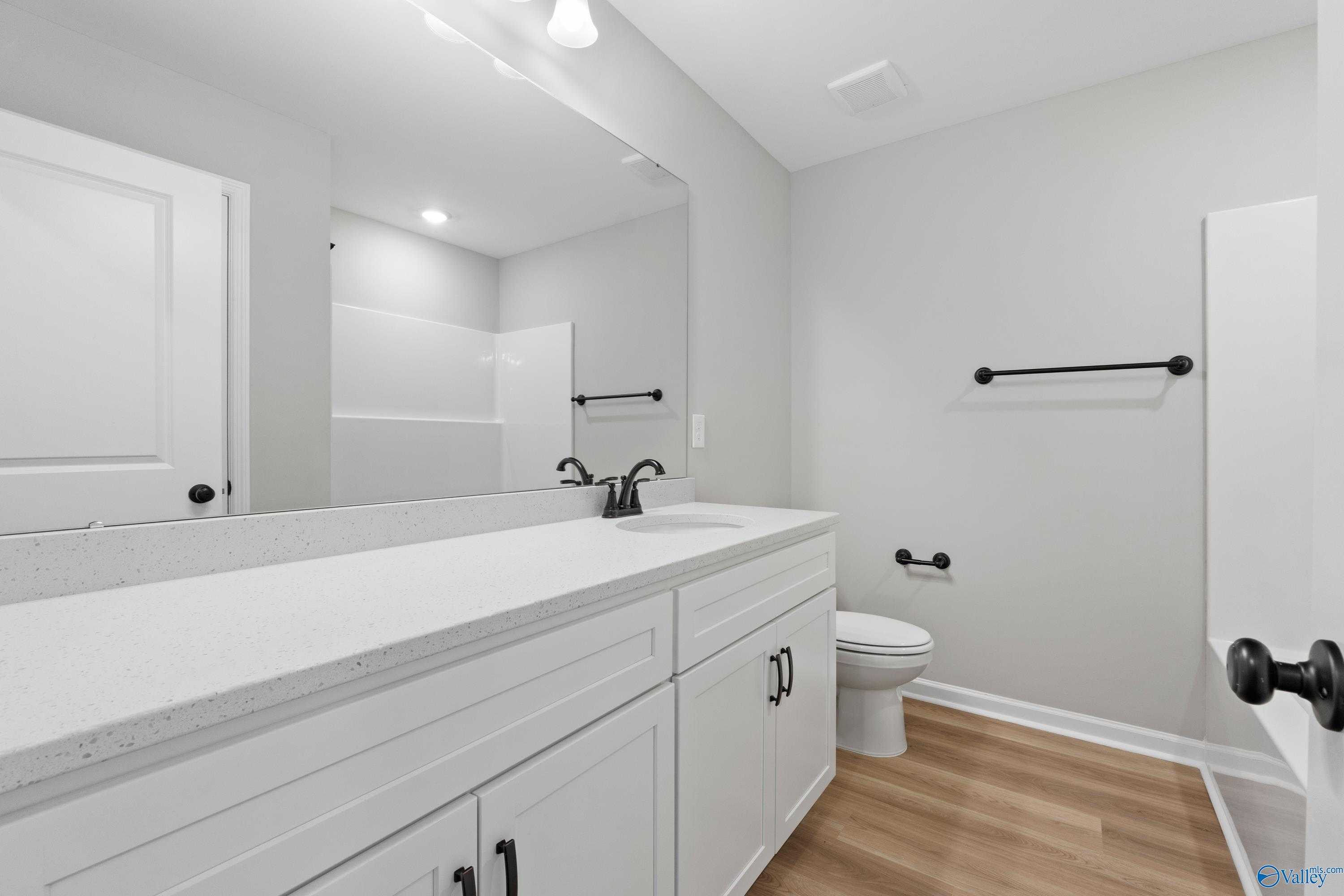 Modern bathroom with white quartz vanity, black faucet, large mirror, toilet, and glass shower in Davidson Homes The Dorado, Huntsville, AL