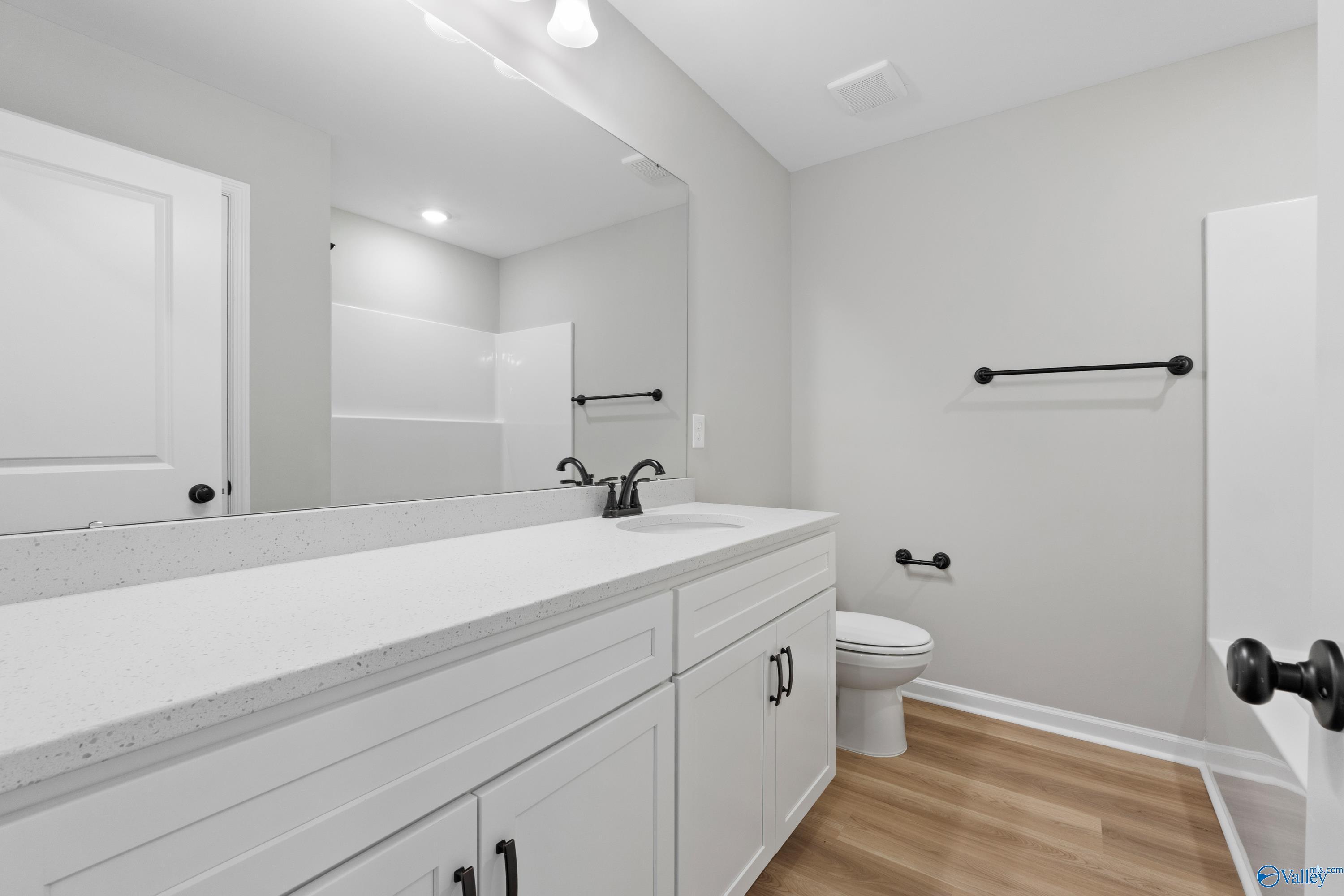 Modern bathroom with white quartz vanity, black faucet, large mirror, toilet, and glass shower in Davidson Homes The Dorado, Huntsville, AL