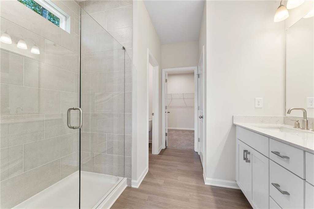 Elegant master bathroom with frameless glass shower, white double vanity, subway tile, and walk-in closet access in Davidson Homes The Ash B plan, Riverwood, Dallas, GA