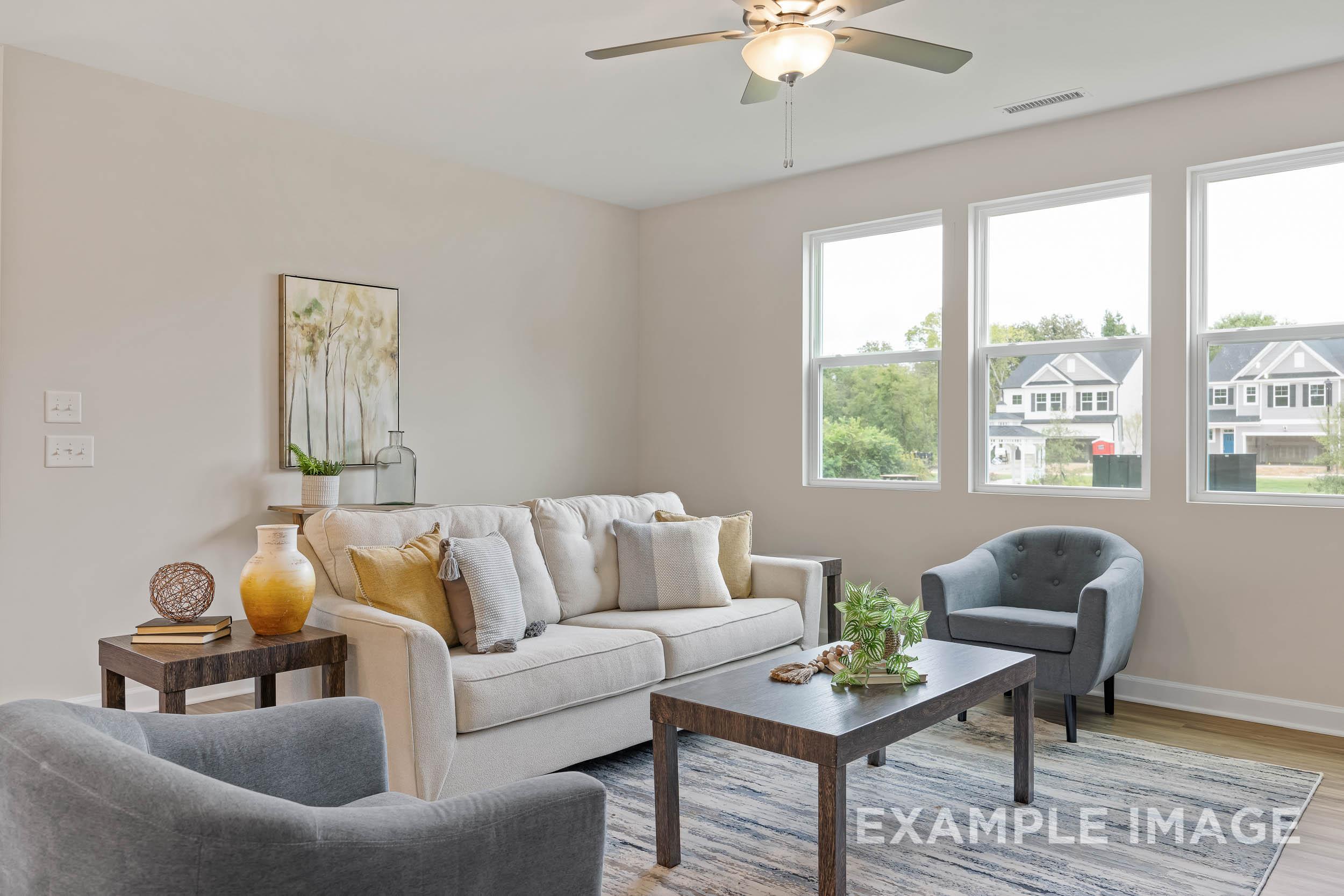 Spacious living room in The Preston B by Davidson Homes featuring beige sofa, large windows with neighborhood view, ceiling fan