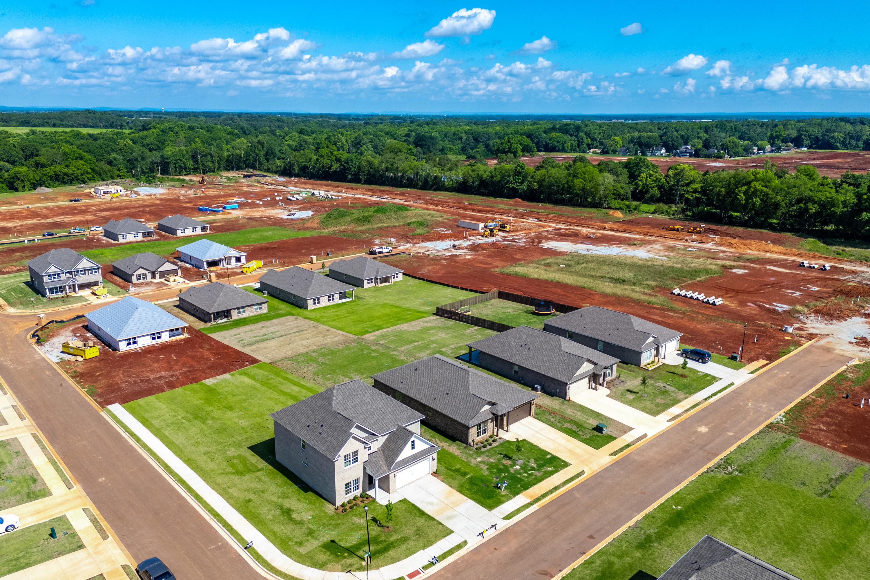 Aerial view of new homes under construction at The Meadows in Athens Alabama with red dirt lots and lush green surroundings