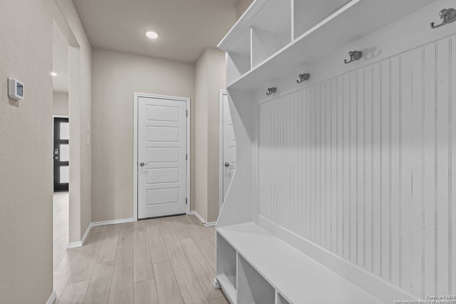 White shiplap mudroom with built-in benches, open shelves, and coat hooks in Davidson Homes The Douglas G, San Antonio, Texas