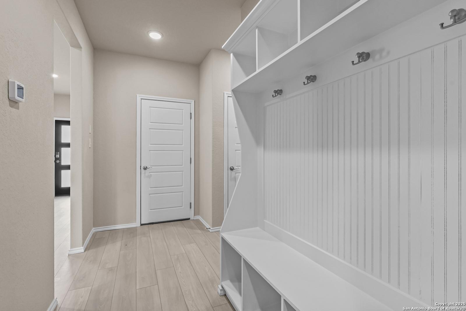 White shiplap mudroom with built-in benches, open shelves, and coat hooks in Davidson Homes The Douglas G, San Antonio, Texas