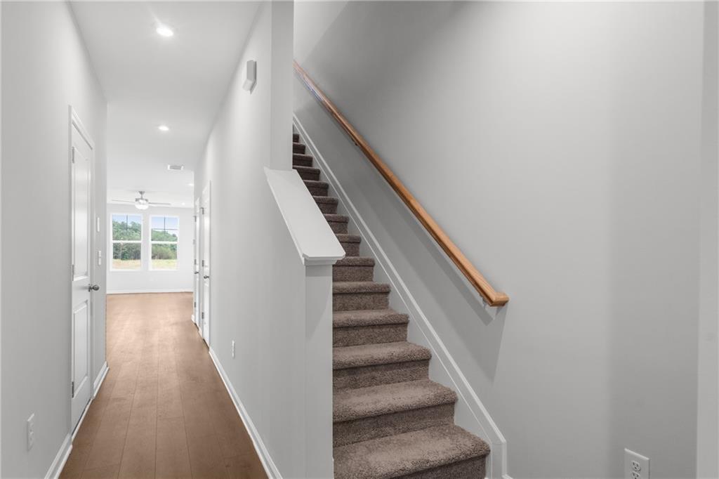 Elegant hallway with light hardwood floors, white walls, bedroom doors, and carpeted staircase in Davidson Homes The Monroe B, Emerson, GA