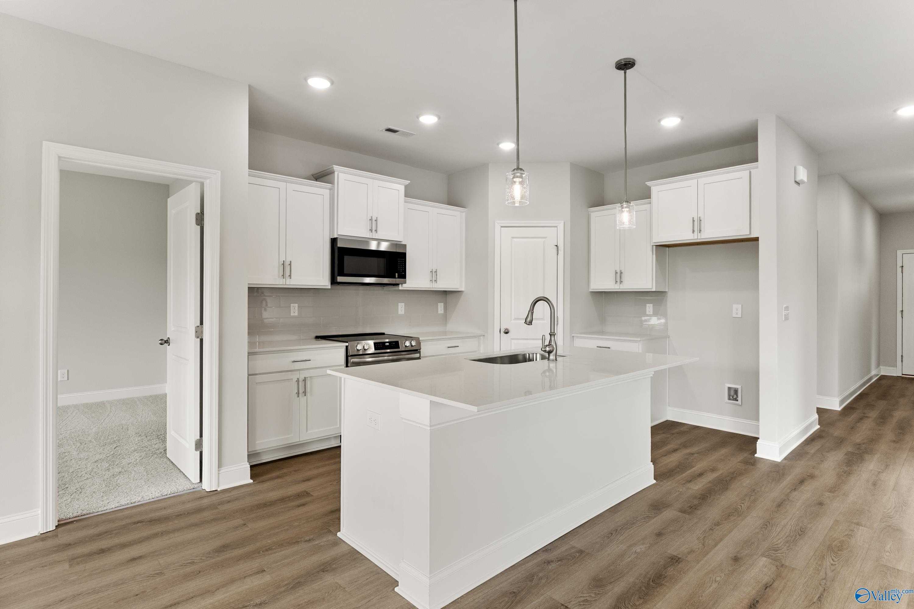 Modern white kitchen with large island, stainless appliances, and open layout in Davidson Homes The Franklin, Athens, Alabama