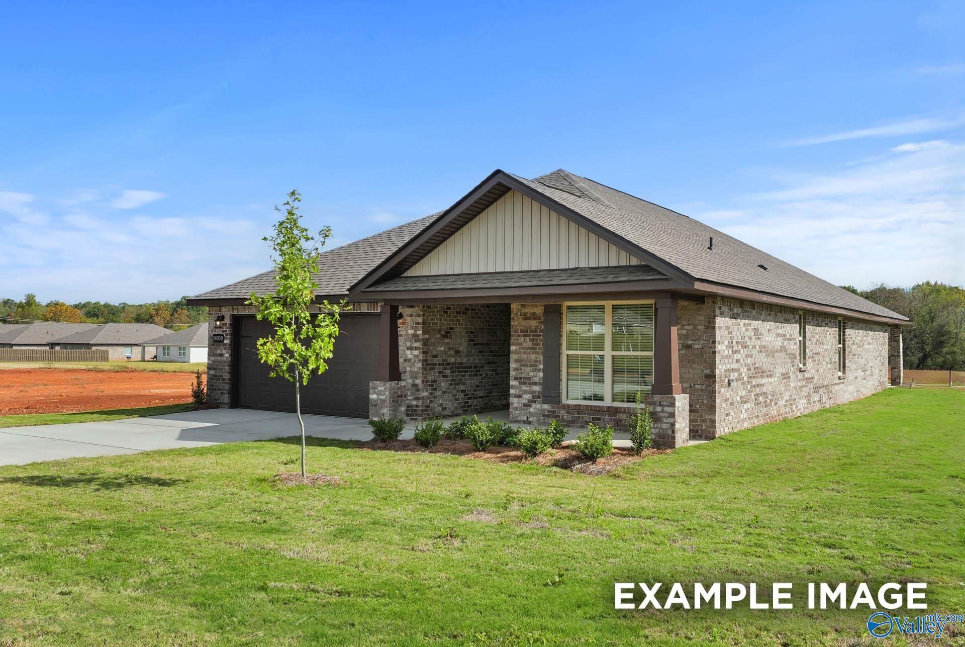Modern brick single-story home with gabled roof, 2-car garage, front porch, and young tree in lush yard, Wood Trail, Toney, Alabama