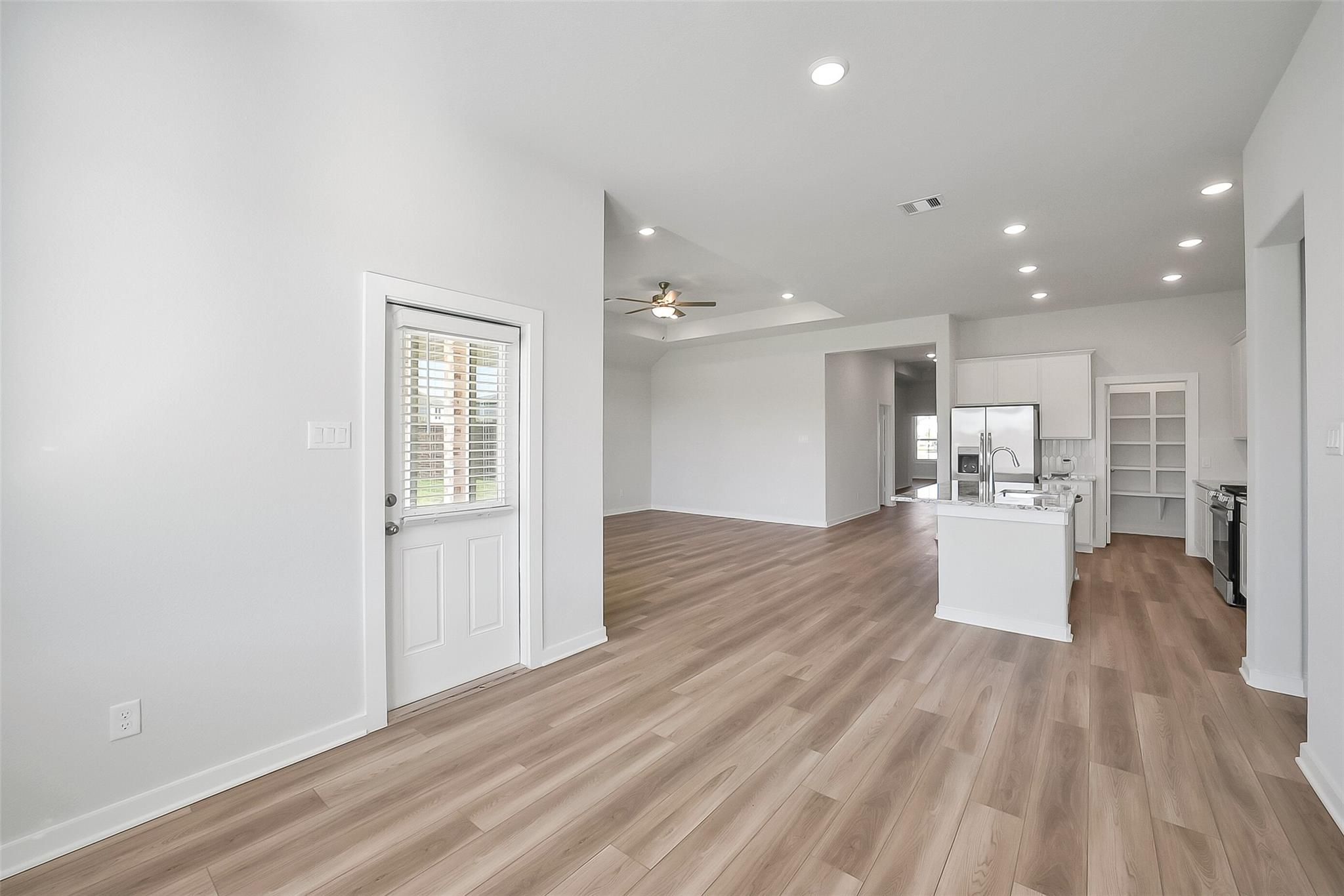 Open-concept kitchen with white island, stainless appliances, wood floors, and ceiling fan in Davidson Homes The Acadia A, Sunterra, Katy, Texas