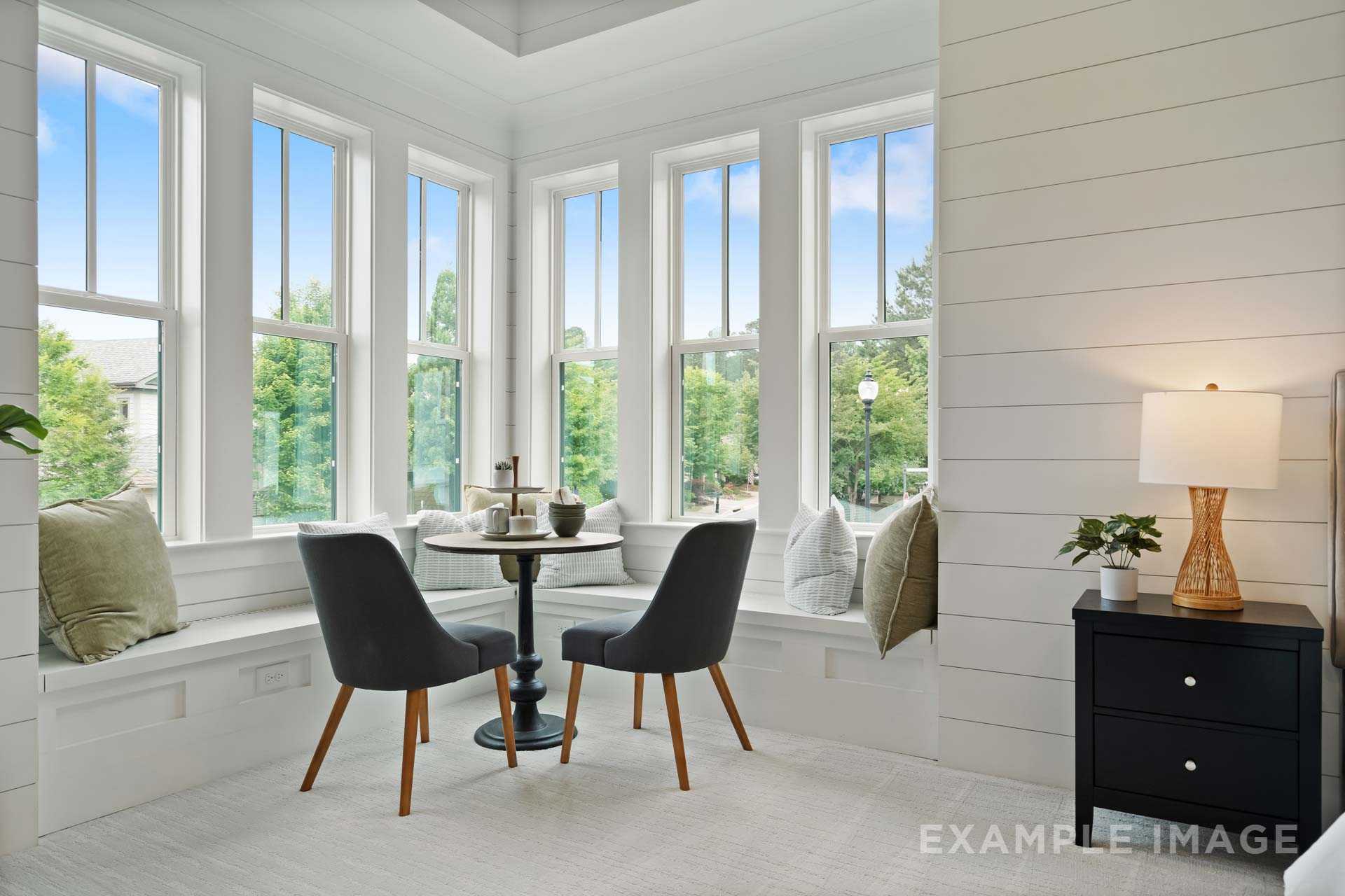 Bright bay window nook in Manor Estates home, Marietta GA with white shiplap walls, round table, chairs, pillows, and plants by Davidson Homes