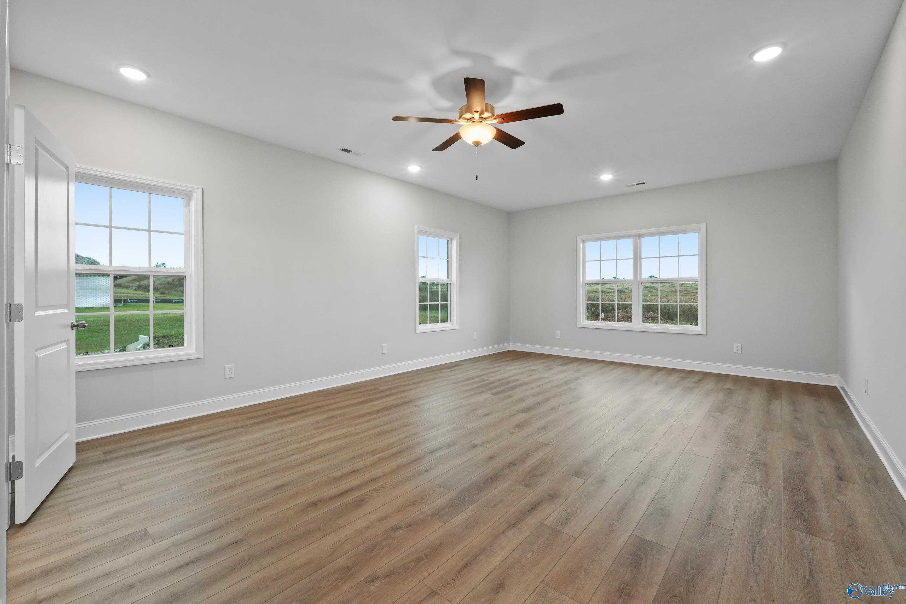 Spacious bedroom with hardwood floors, ceiling fan, and scenic field views through large windows in The Lanier home, Harvest, AL