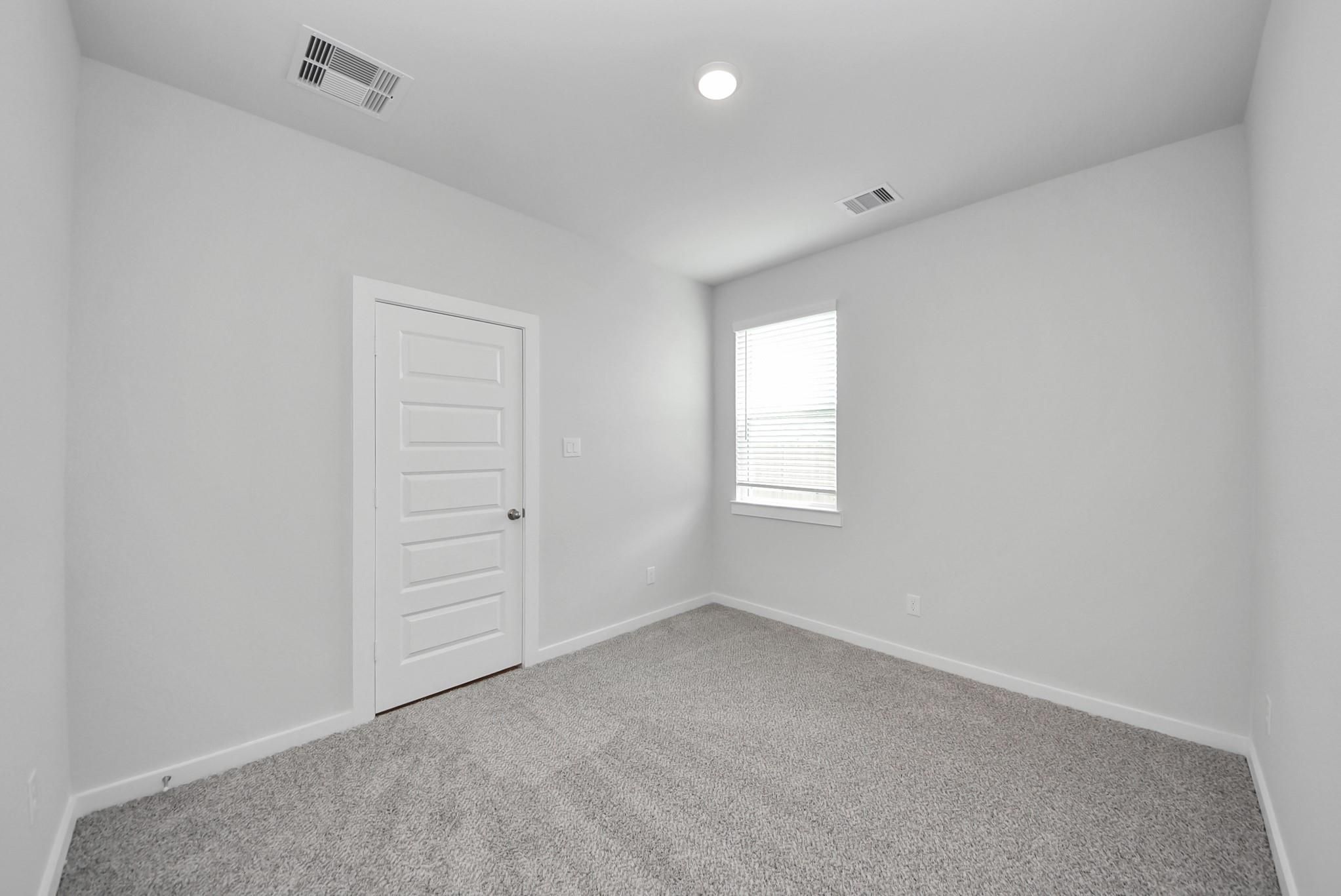 Bright empty bedroom with plush gray carpet, white door, and window with blinds in Davidson Homes San Marcos E, Beasley, Texas