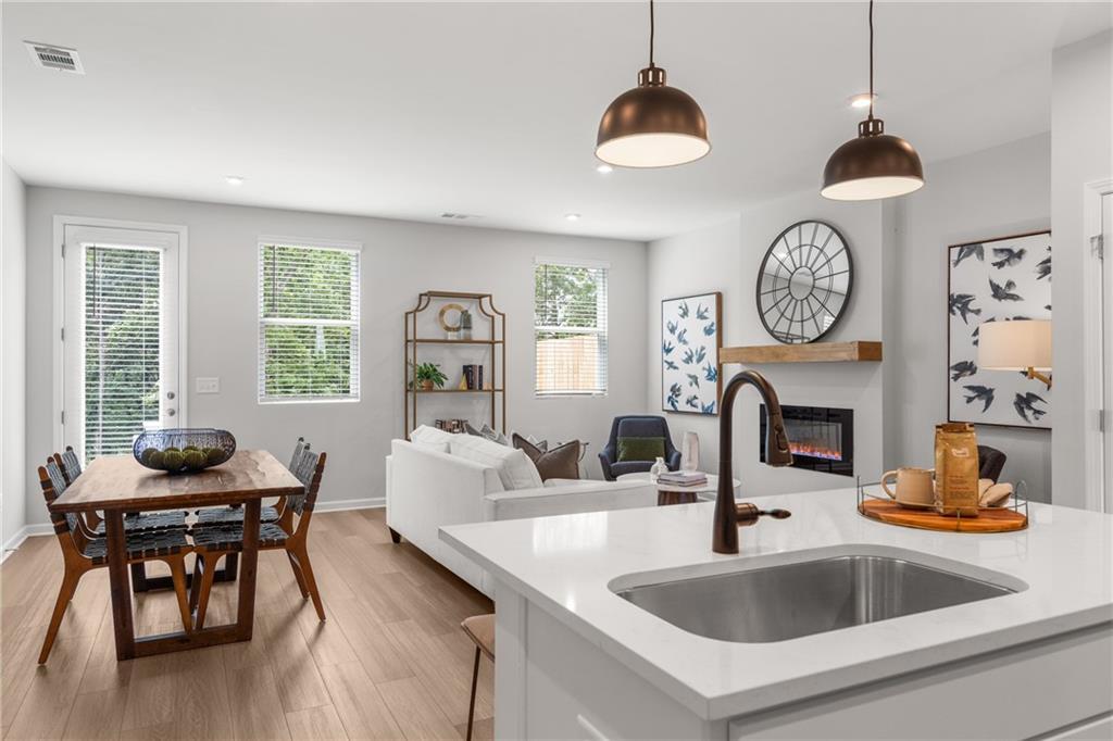 Open-concept living-dining area with white sofa, gas fireplace, wooden table, kitchen island, and pendant lights in Davidson Homes The Durant A, Emerson, Georgia