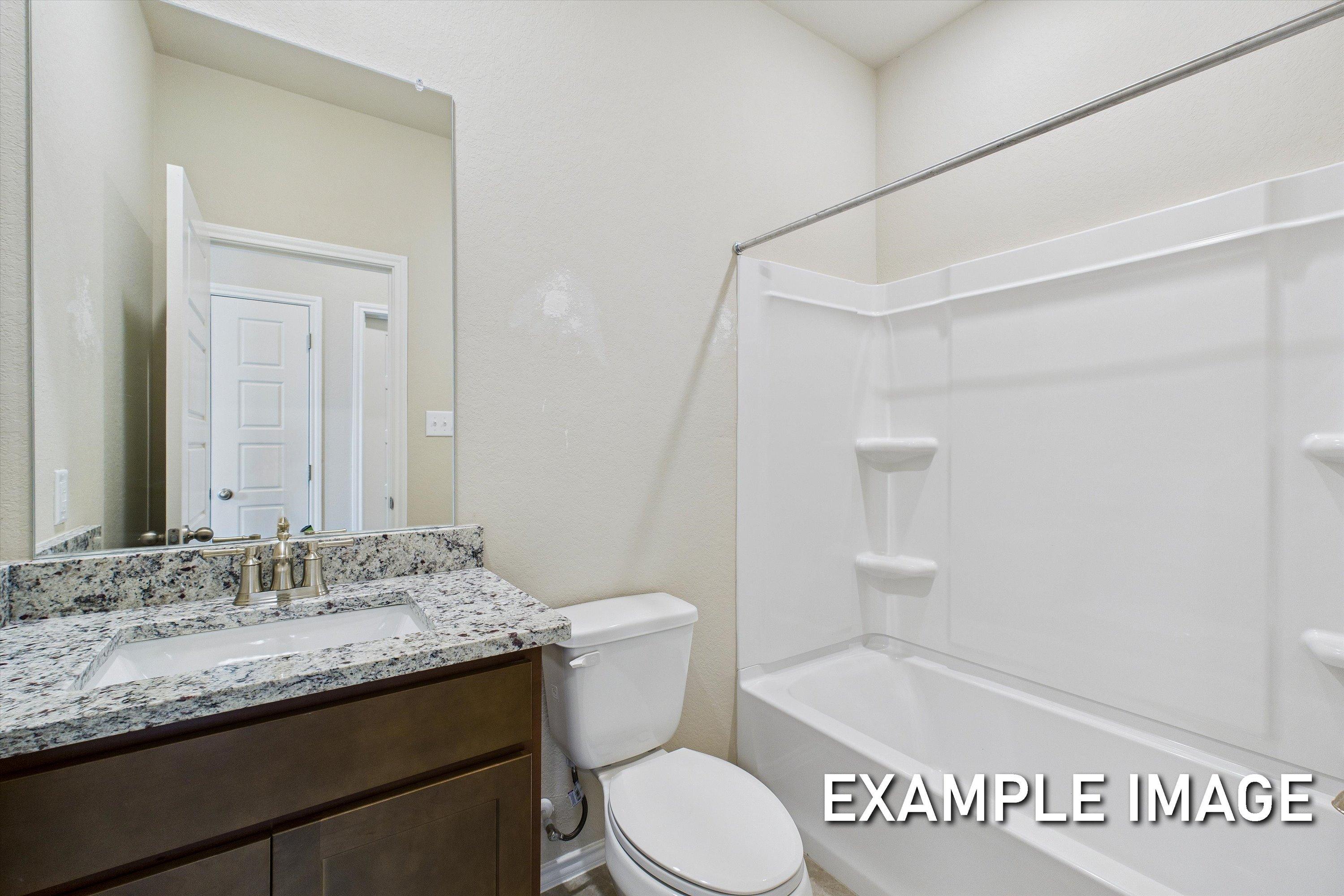 Modern bathroom in The Comal featuring a granite vanity, dark wood cabinetry, and a clean white tub-shower combination.