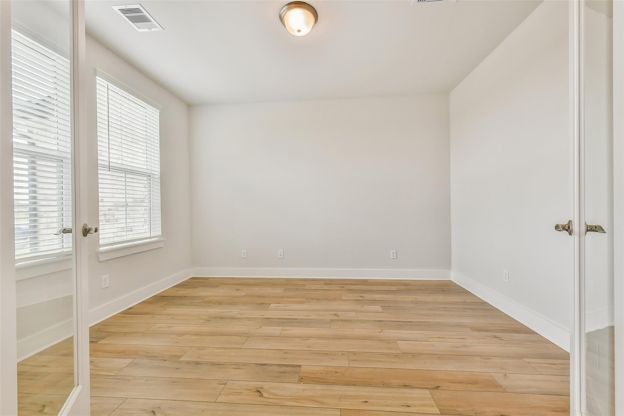 Bright empty bedroom with light oak hardwood floors, white walls, large windows with blinds in Davidson Homes The Victoria A, Lago Mar