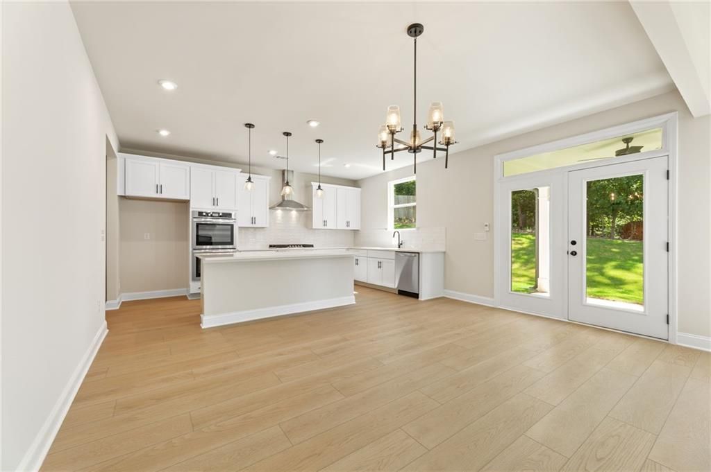 Modern open-concept kitchen with white cabinets, stainless appliances, island, and French doors to backyard in The Hickory E, Buford, GA