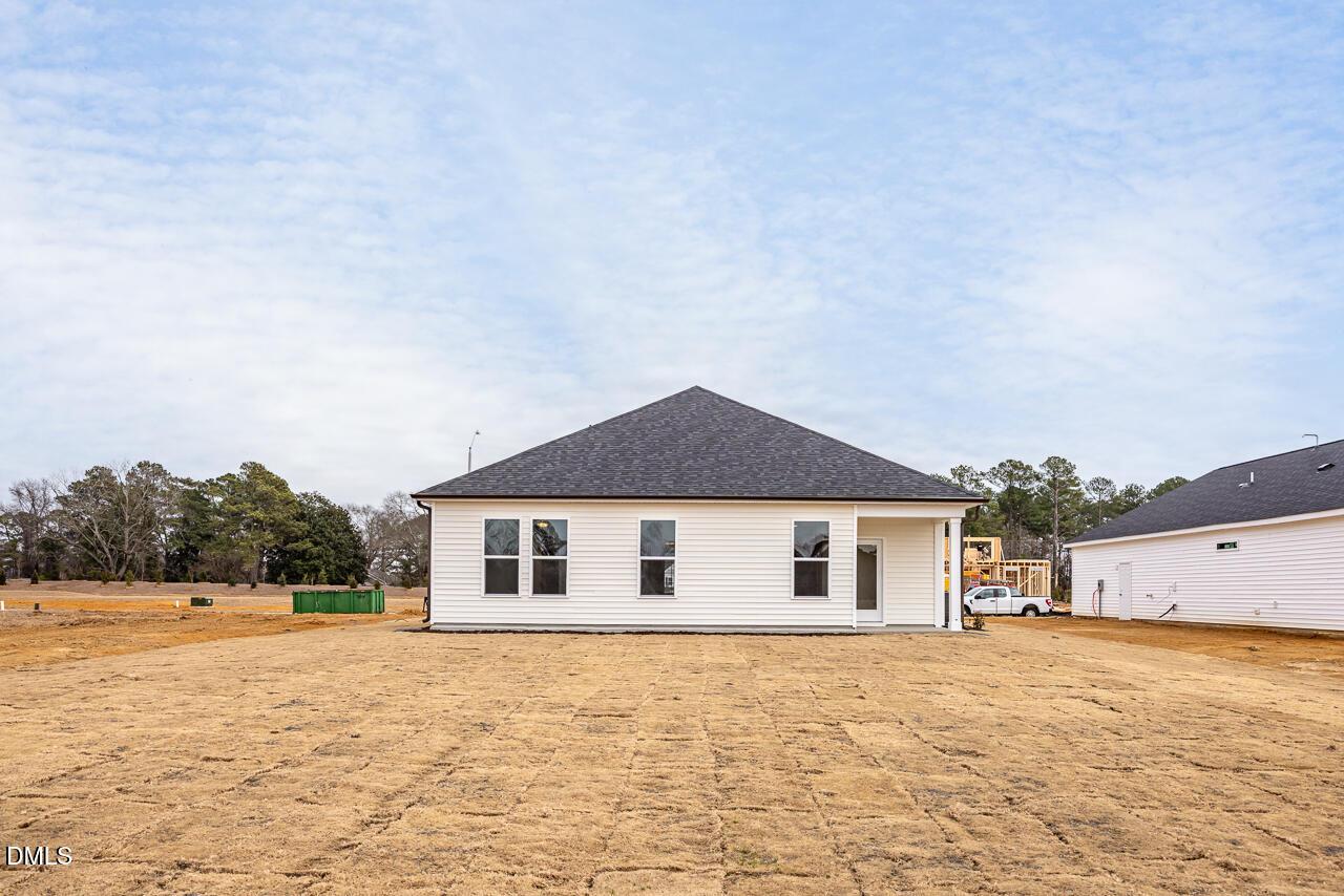 Modern white single-story home with gable roof, covered porch, and windows on dirt lot in Retreat at North Main, Lillington, North Carolina