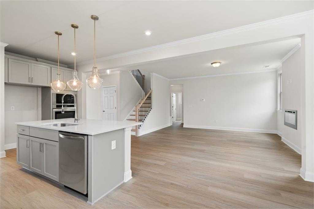 Modern open kitchen with white cabinets, stainless appliances, large island, and pendant lights in The Willow D home, Wehunt Meadows, Hoschton, Georgia
