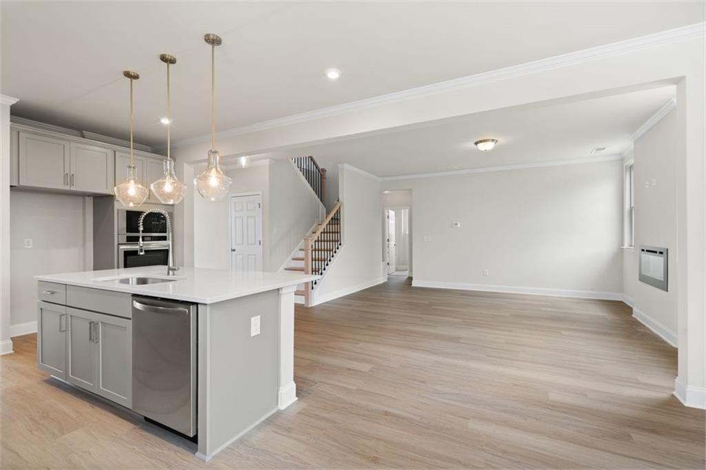 Modern open kitchen with white cabinets, stainless appliances, large island, and pendant lights in The Willow D home, Wehunt Meadows, Hoschton, Georgia