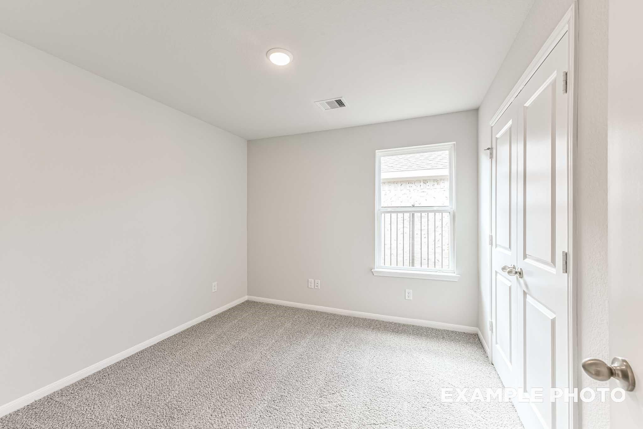 Bright carpeted secondary bedroom with closet in The Laguna C floor plan by Davidson Homes in Sunterra, Katy, Texas.