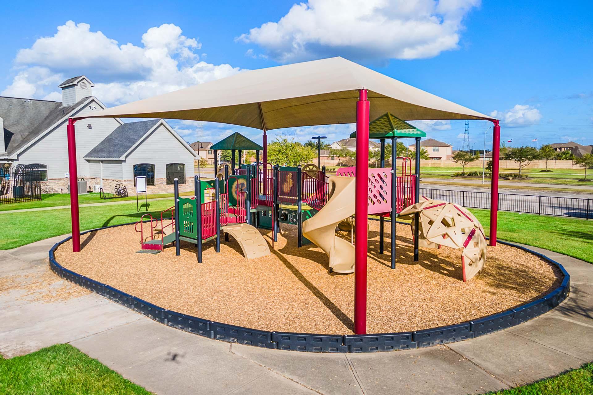 Children's playground at Sierra Vista in Rosharon Texas with colorful slides climbing structures and shaded canopy by Davidson Homes