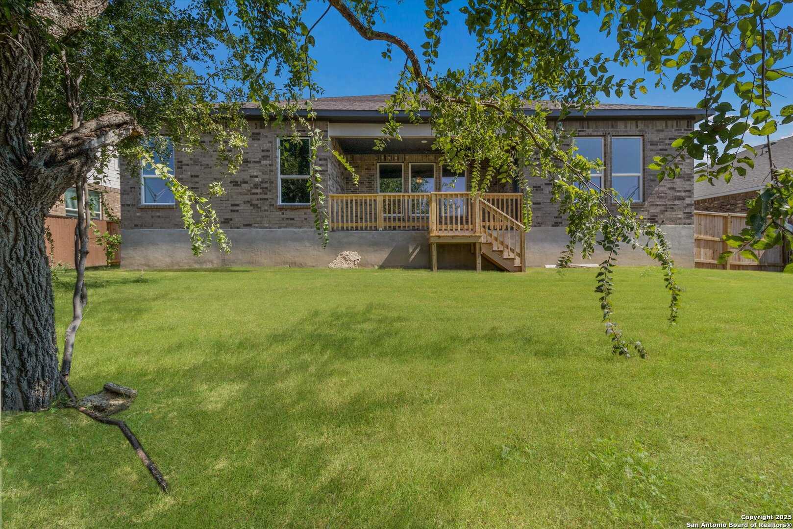 Two-story brick home backyard with wooden deck, stairs, lush green lawn in Davidson Homes The Jennings H, Ladera, San Antonio