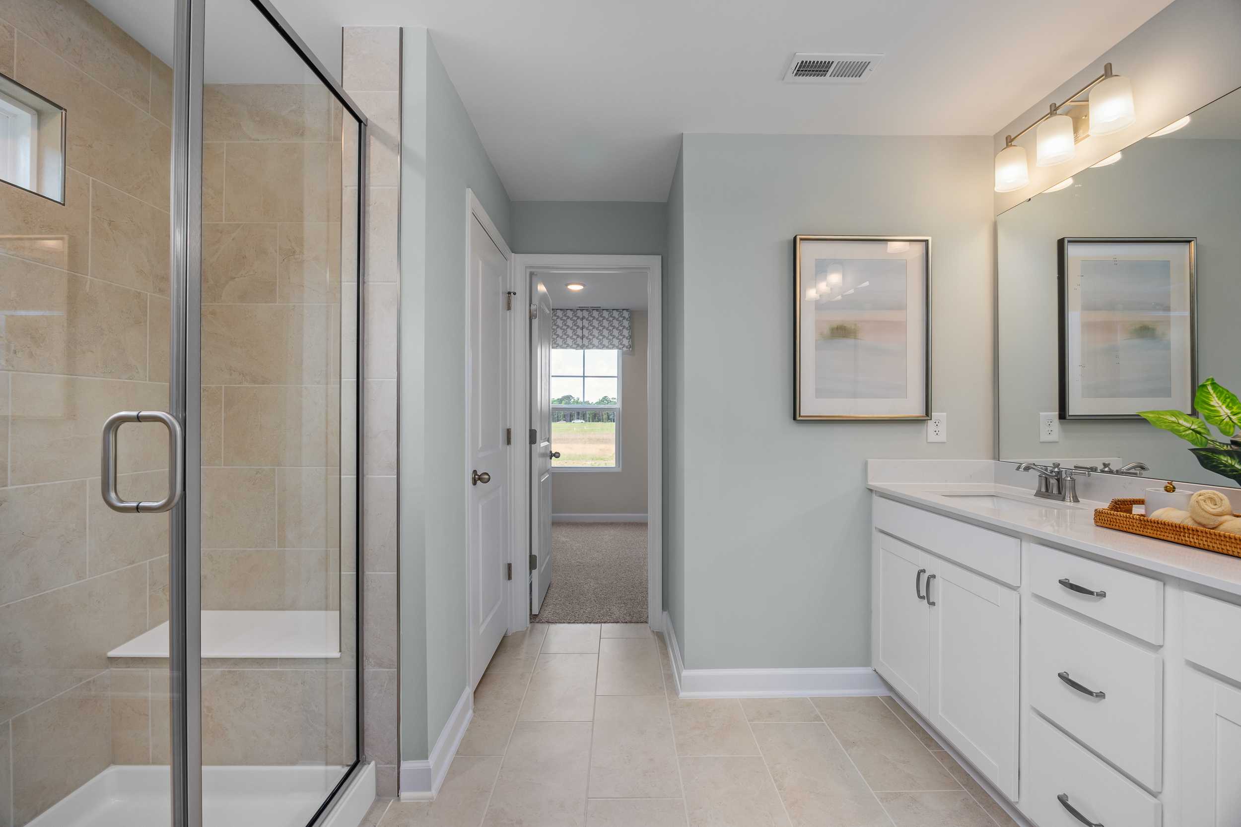 Spacious primary bathroom with glass walk-in shower, double white vanity, and soft lighting at Retreat at North Main in Lillington NC by Davidson Homes