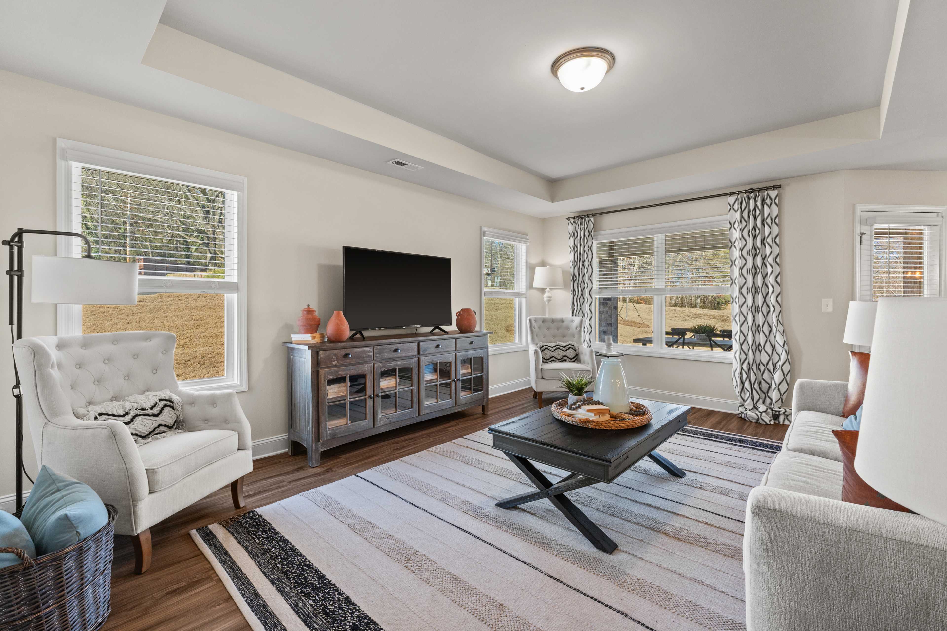 Spacious living room at Ramsay Cove in Owens Cross Roads AL featuring gray media console, plush gray sofa, hardwood floors, and large windows