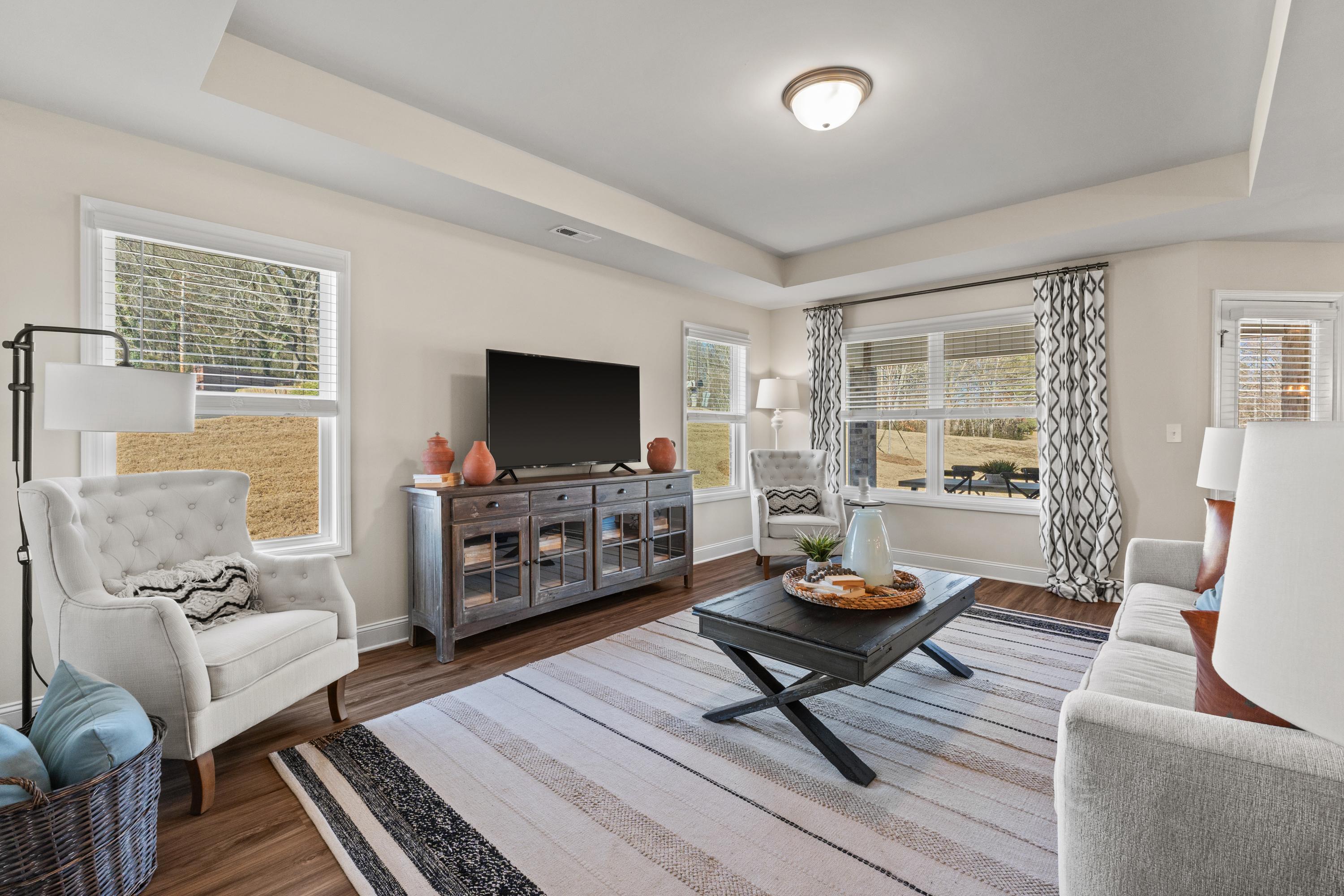 Spacious living room at Berry Cove in New Market Alabama with gray sofa hardwood floors large windows and neutral decor