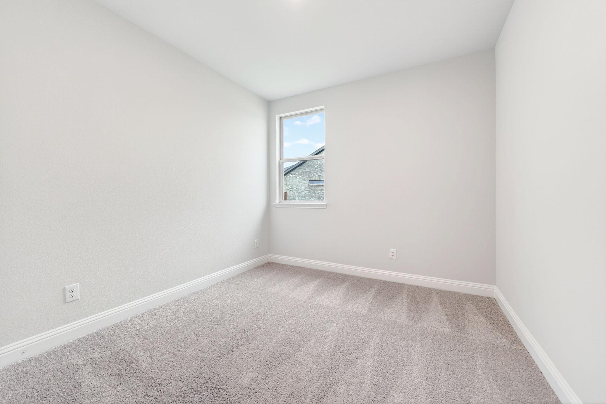 Bright, carpeted bedroom in The Redbud home design by Davidson Homes featuring neutral walls and natural lighting.