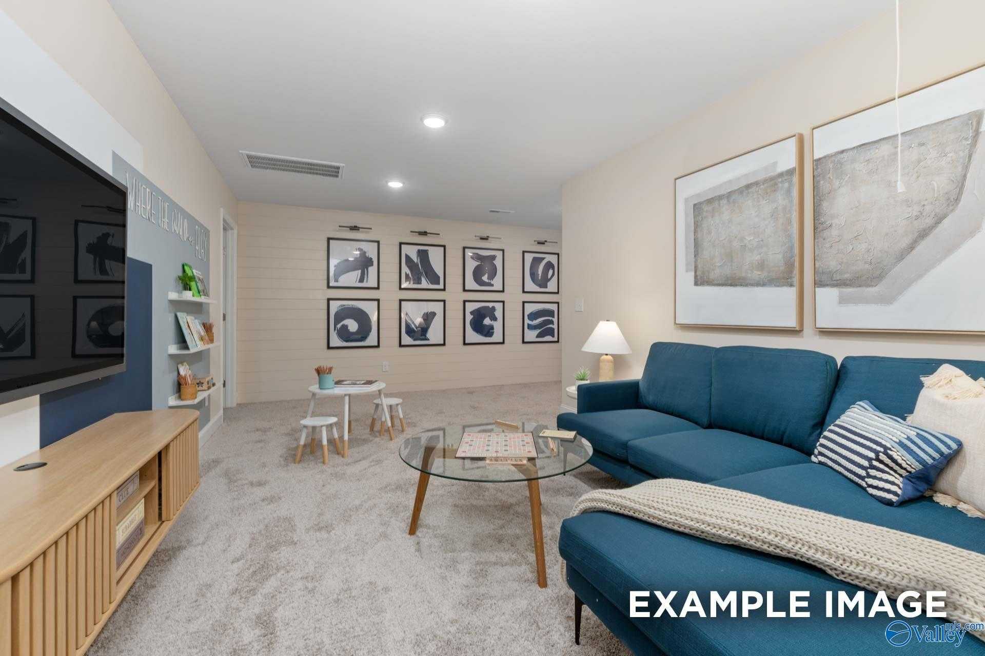 Cozy media room featuring mounted TV, blue sectional sofa, glass coffee table, and kids' play area in Davidson Homes The Camden B, Huntsville, Alabama