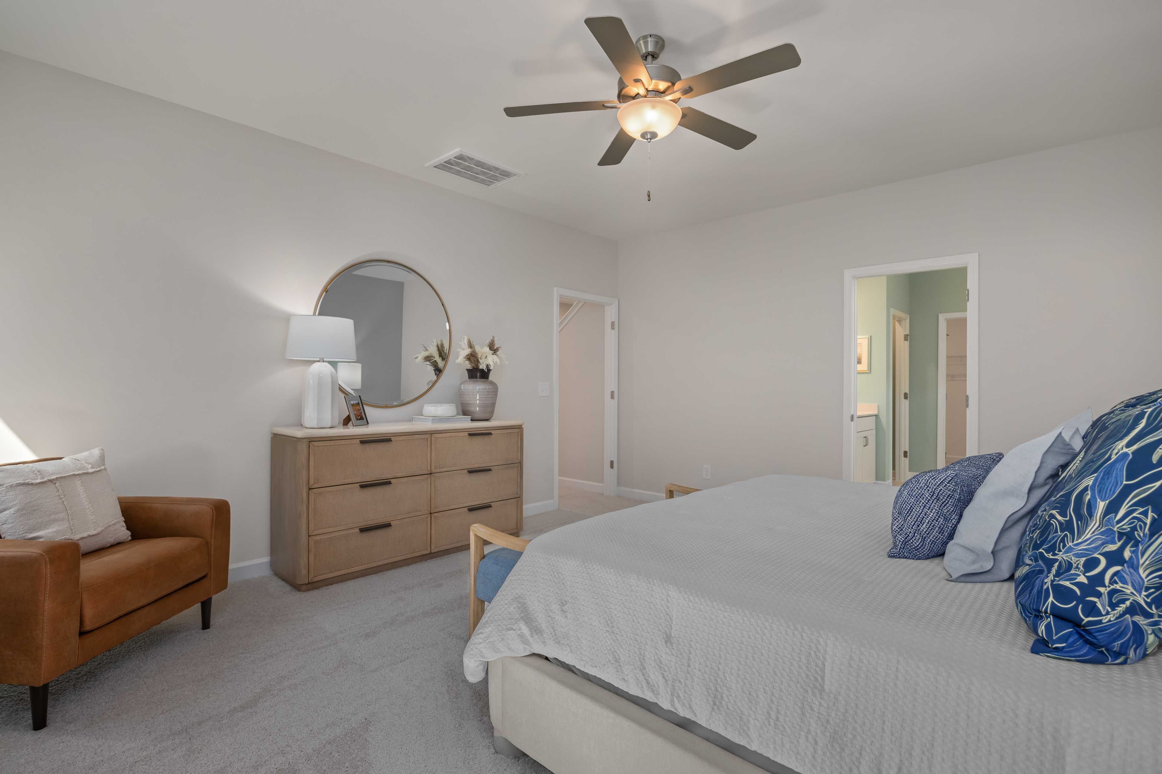 Spacious master bedroom at Sage on North Main in Wake Forest NC with king bed, ceiling fan, leather armchair, and en-suite door