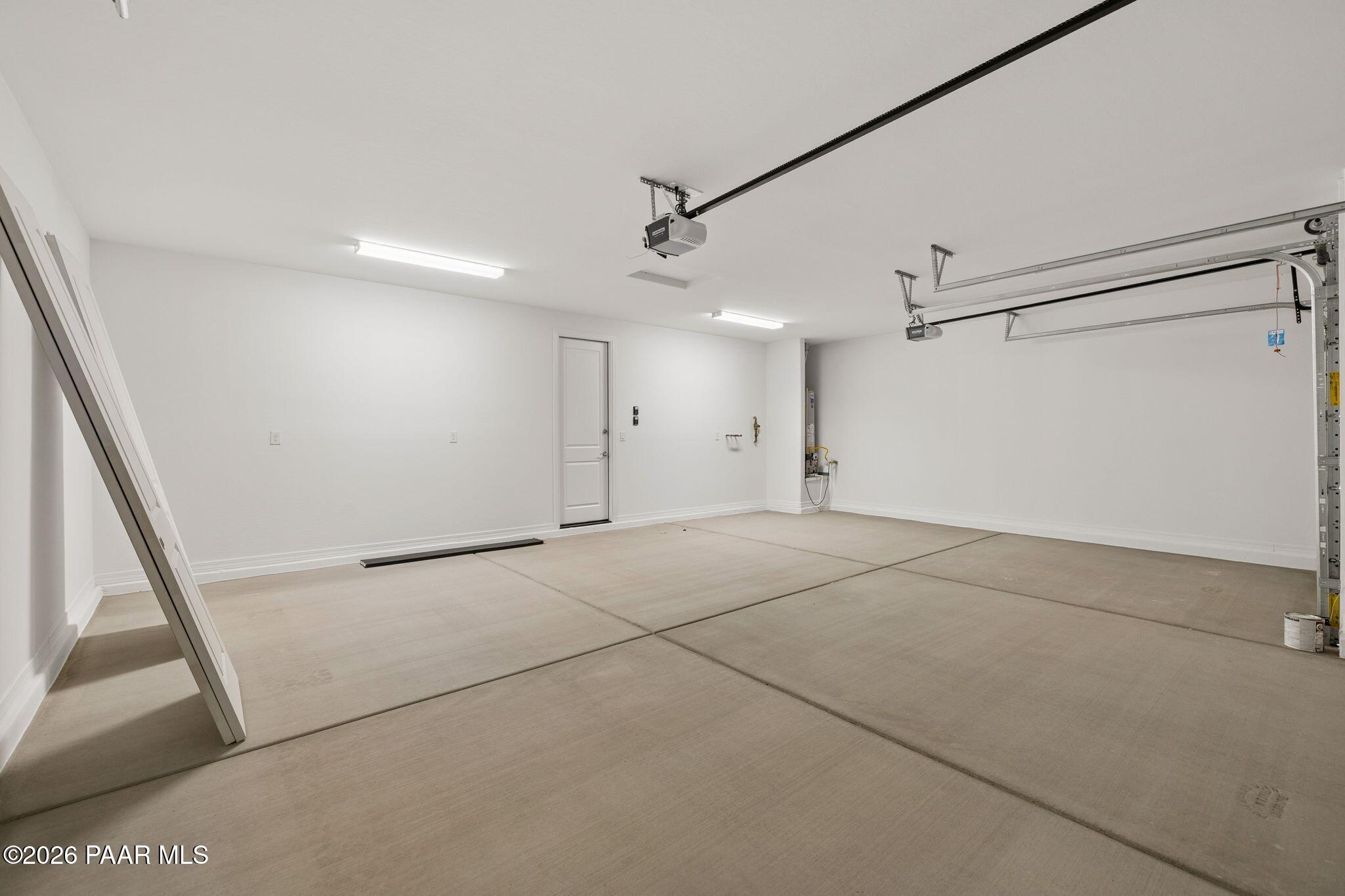 Spacious 3-car garage with white walls, stained concrete floor, and overhead opener in Davidson Homes The Monarch A, Prescott, Arizona