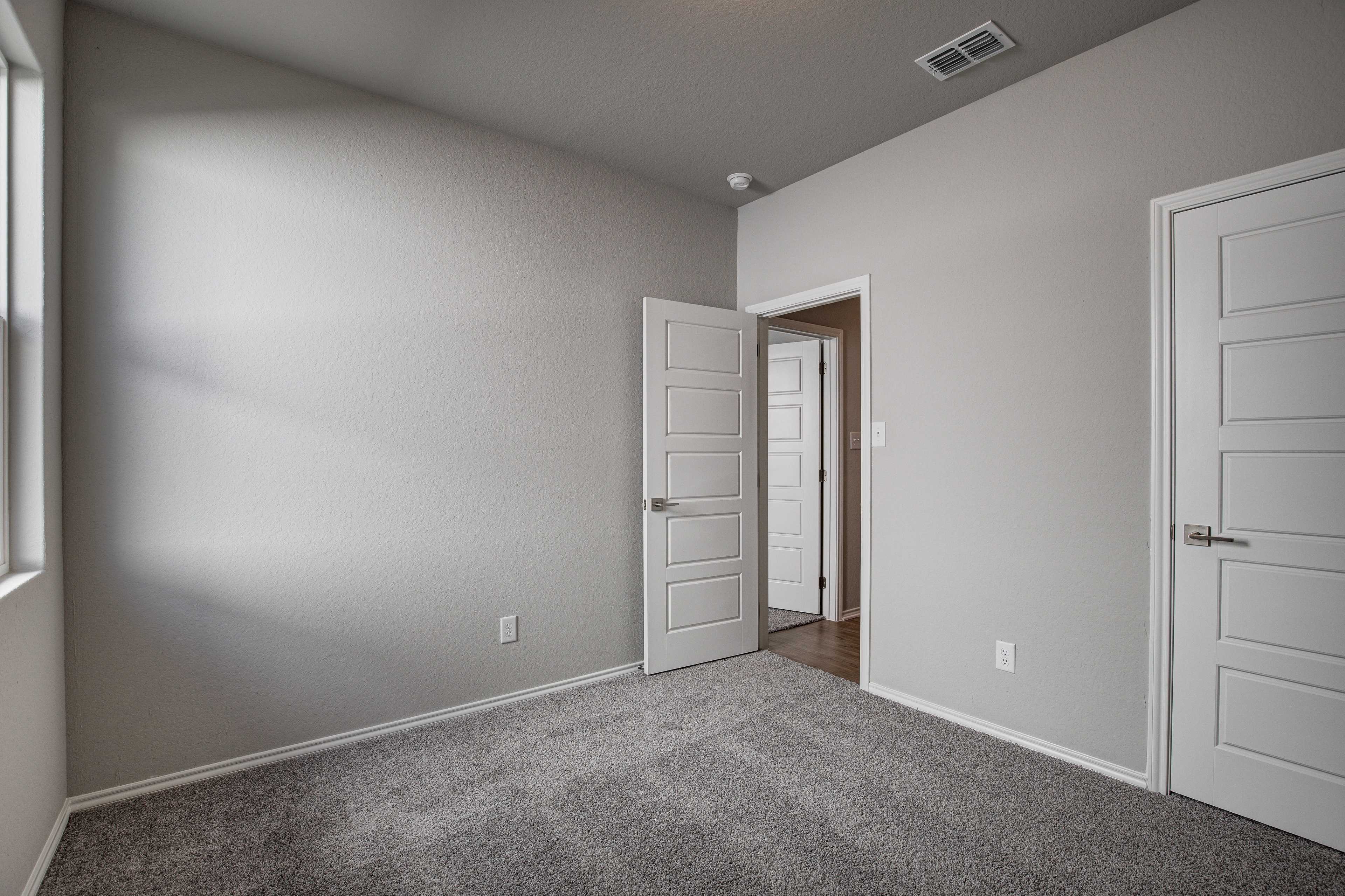 Spacious secondary bedroom in The Frio B home design with gray walls, white doors, carpeted floor, and natural light