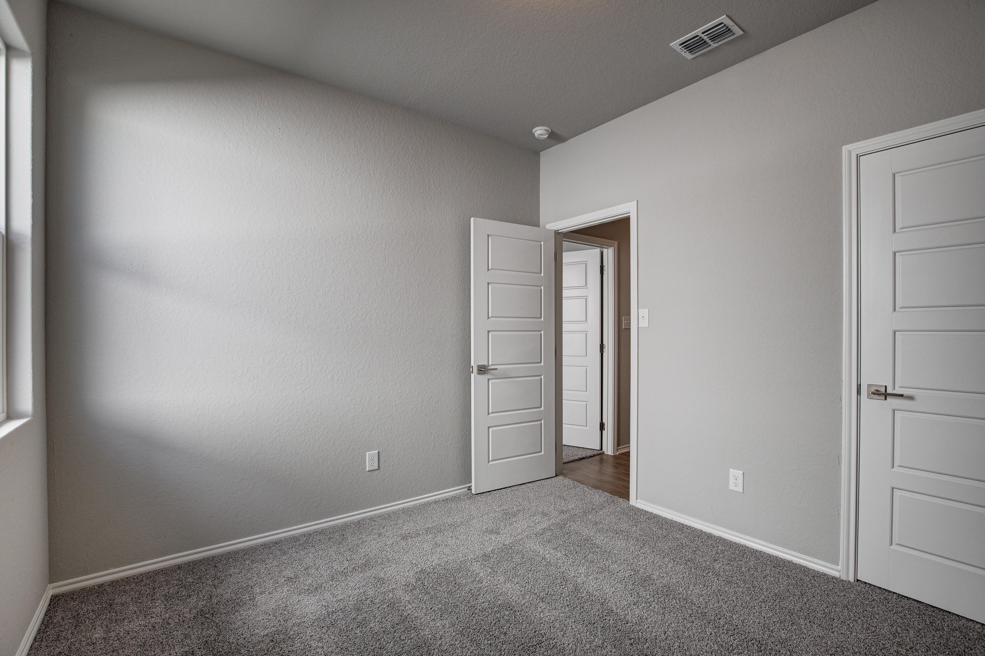 Spacious secondary bedroom in The Frio Davidson Homes design with gray walls, carpet flooring, double doors, and natural light