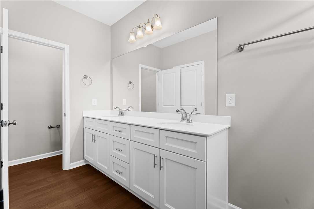 Elegant master bathroom with double sink vanity, white shaker cabinets, large mirrors, and sconce lighting in Evermore Homes The Orion, Cusseta, Alabama