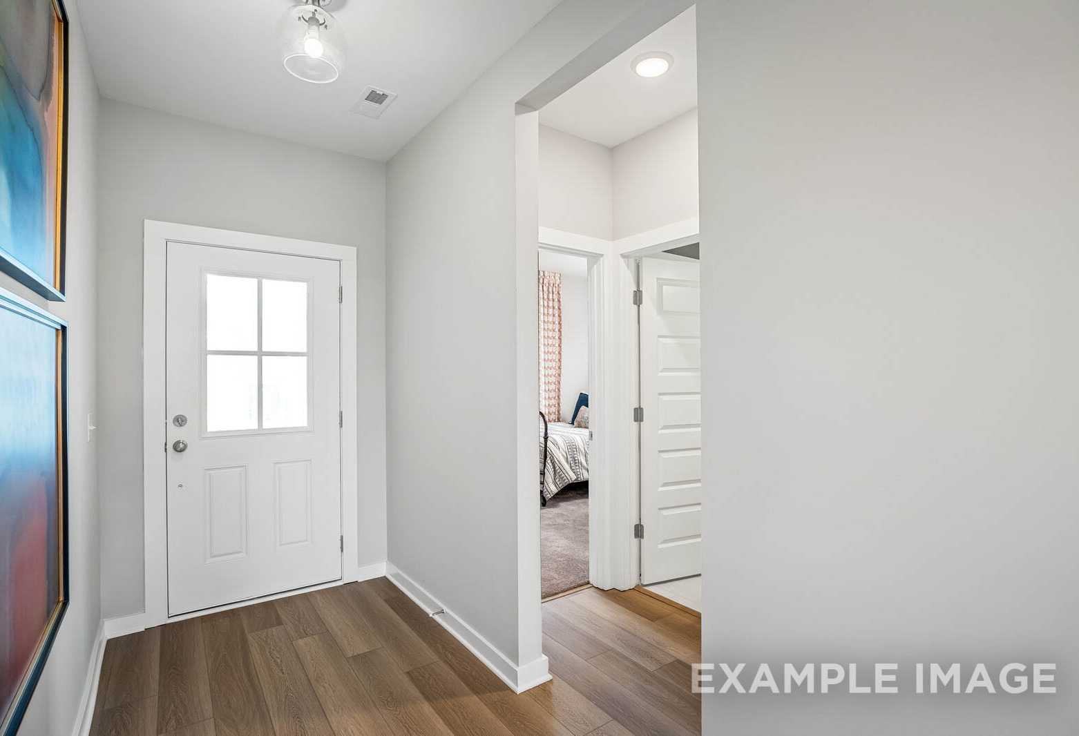 Spacious entryway in The Franklin C home design with white paneled door, light wood floors, and master bedroom glimpse