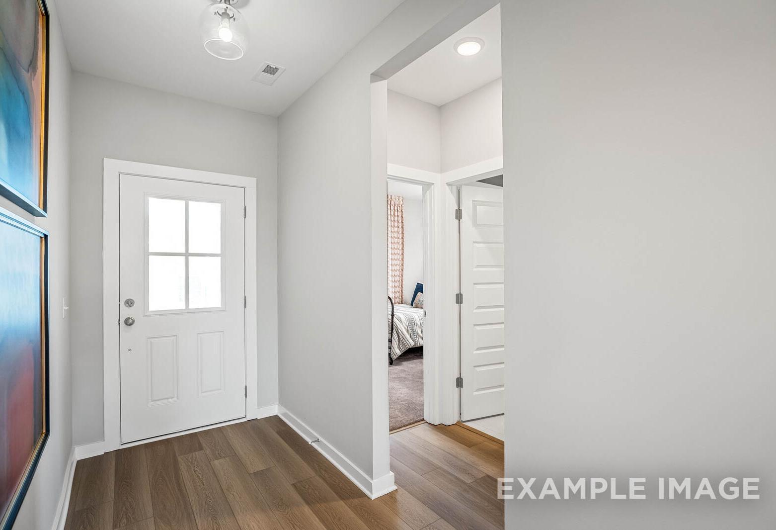 Spacious entryway in The Franklin C home design with white paneled door, light wood floors, and master bedroom glimpse