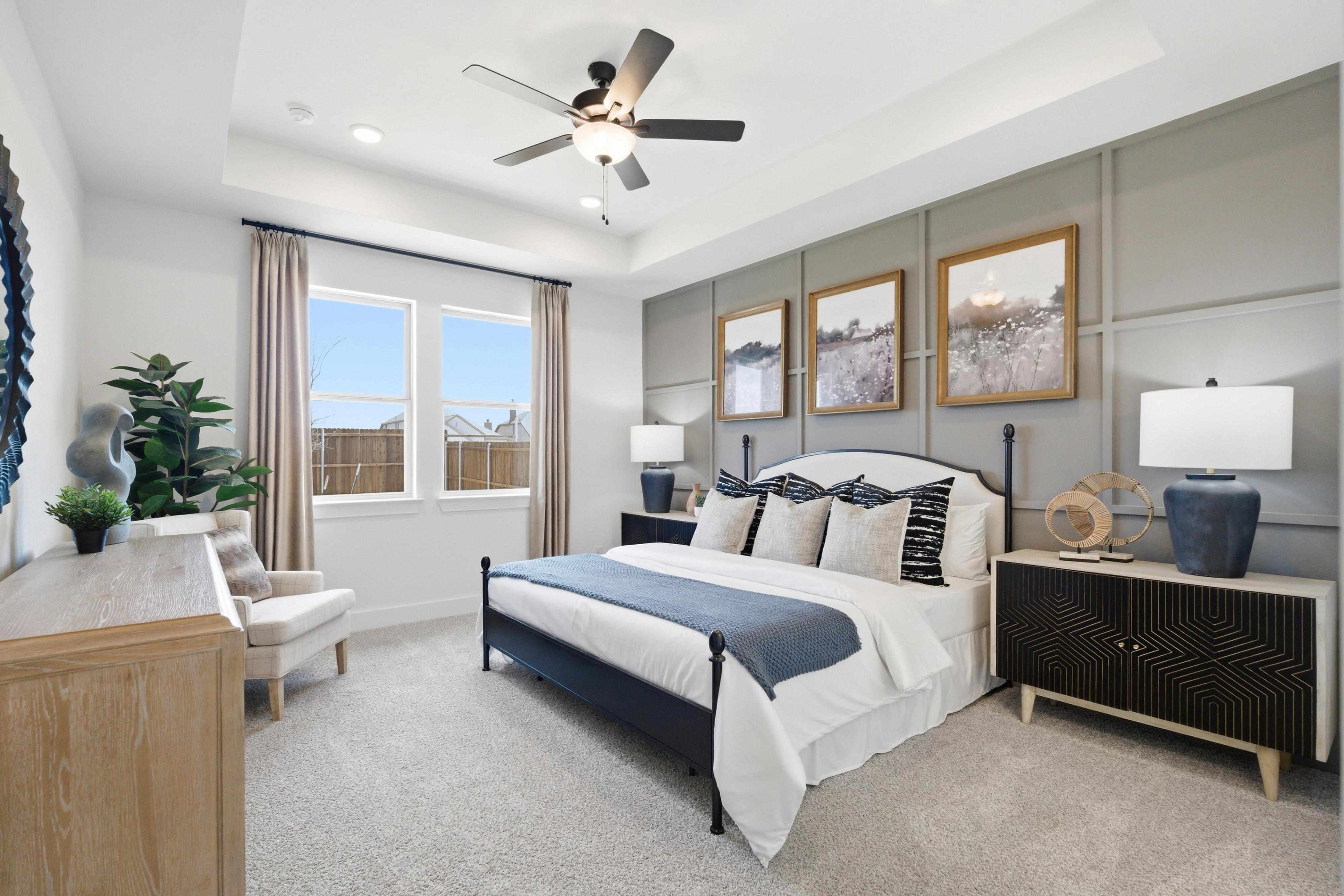 Spacious primary bedroom in Mercer Meadows, Royse City TX with king bed, gray accent wall, artwork, and ceiling fan