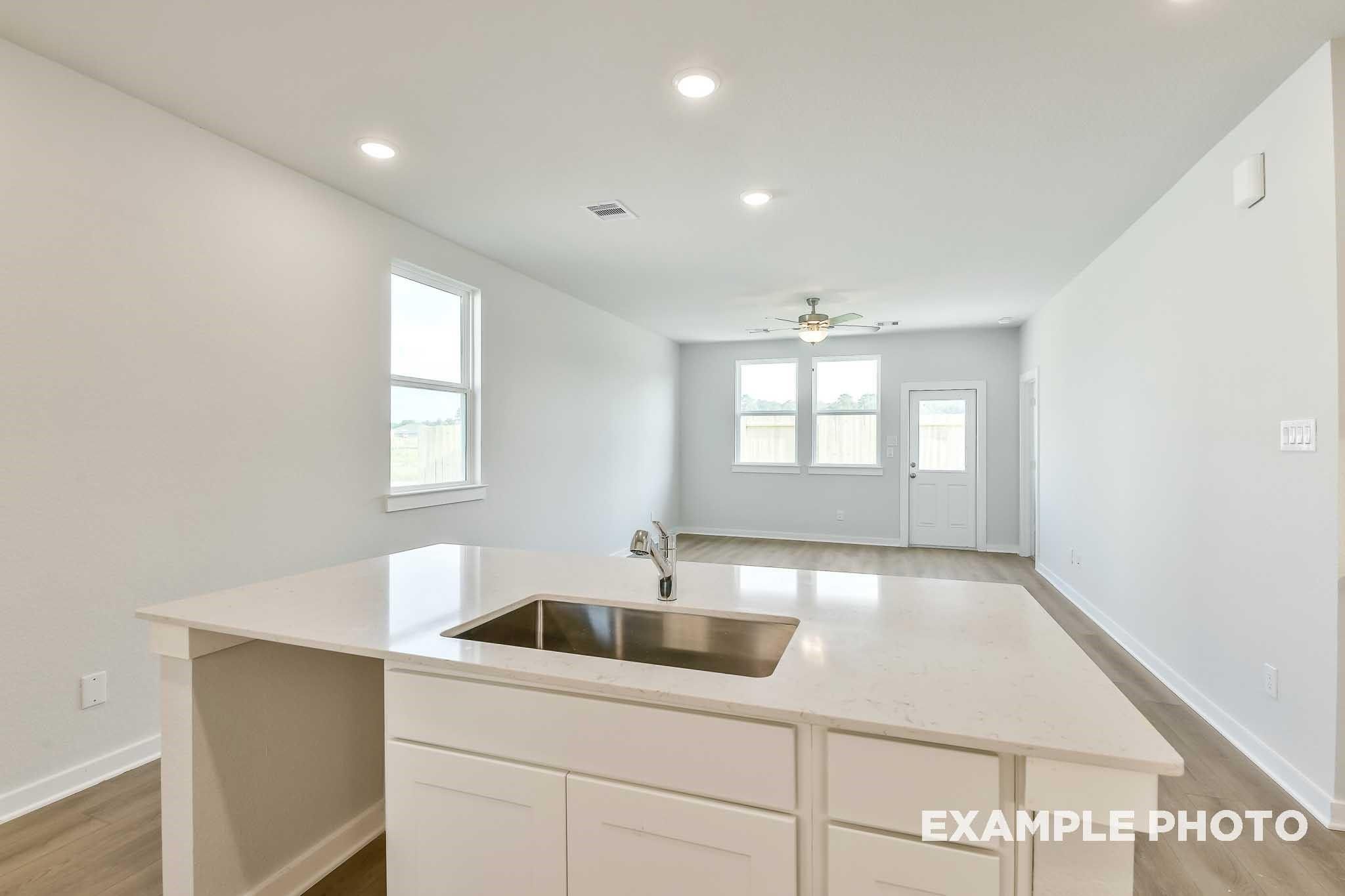 Modern white kitchen island with sink and cabinets in open-concept living area, Davidson Homes The Colorado G, Conroe, Texas