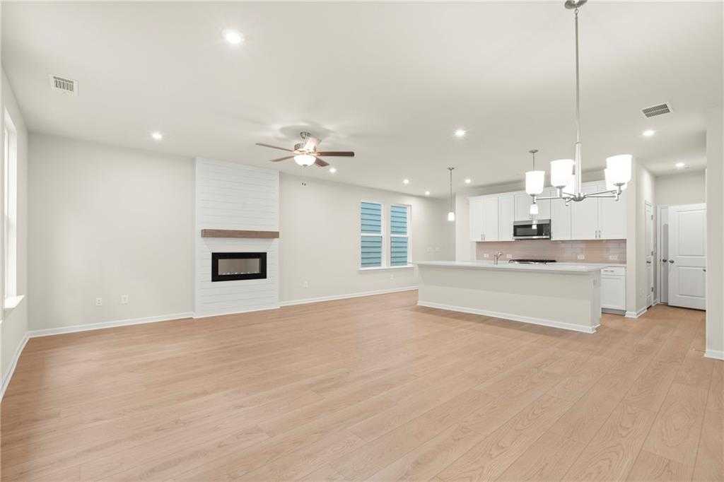 Open-concept living room with white brick fireplace, ceiling fan, and chandelier next to modern white kitchen in Davidson Homes Cary A, Kennesaw, GA