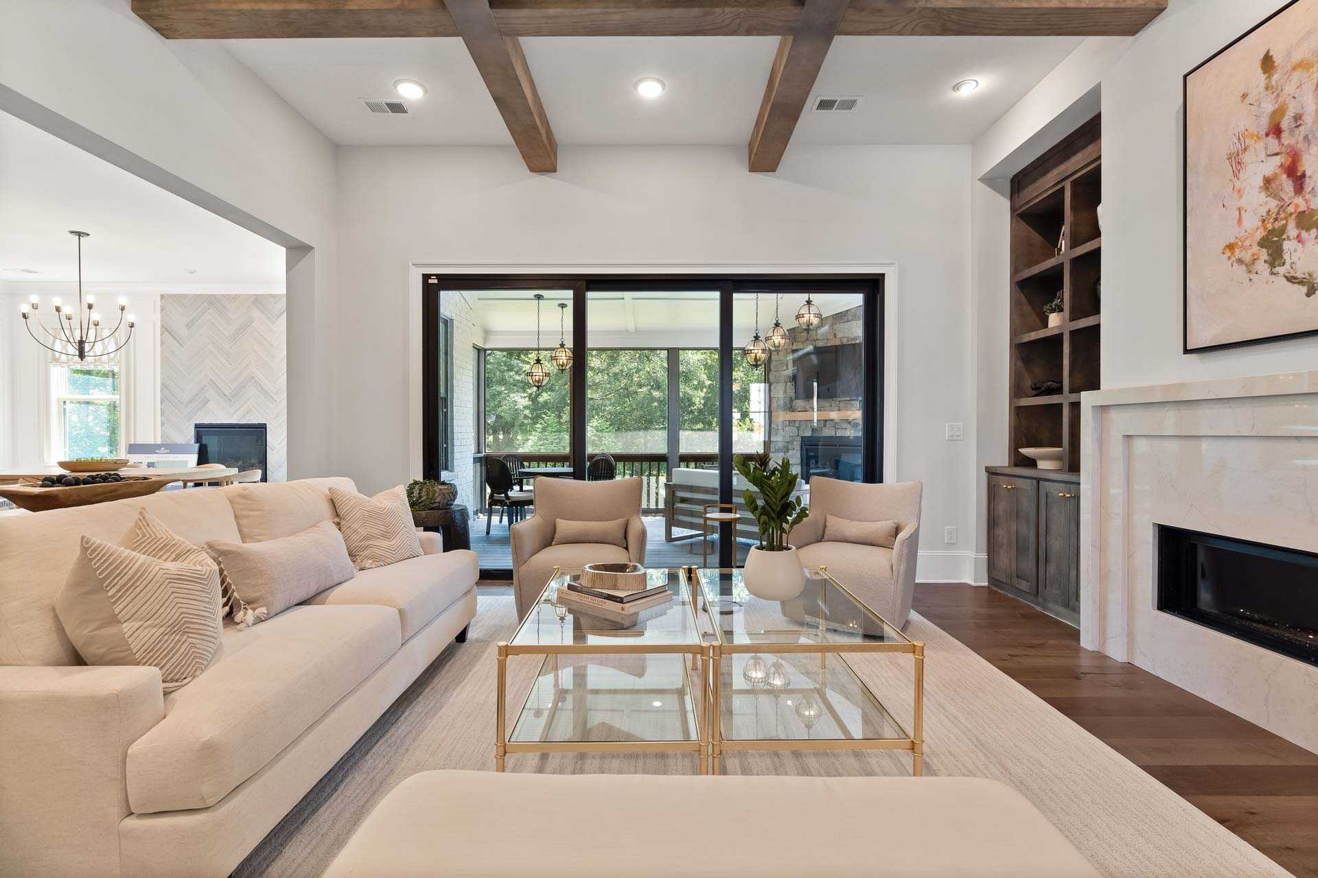 Elegant open-concept living room in Tanglewood East Cobb GA with exposed wood beams, beige sofas, marble fireplace, and sliding doors to patio