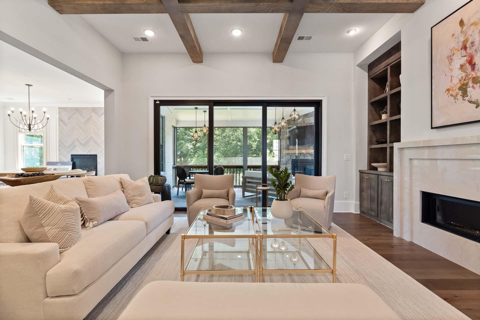 Elegant open-concept living room in Tanglewood East Cobb GA with exposed wood beams, beige sofas, marble fireplace, and sliding doors to patio