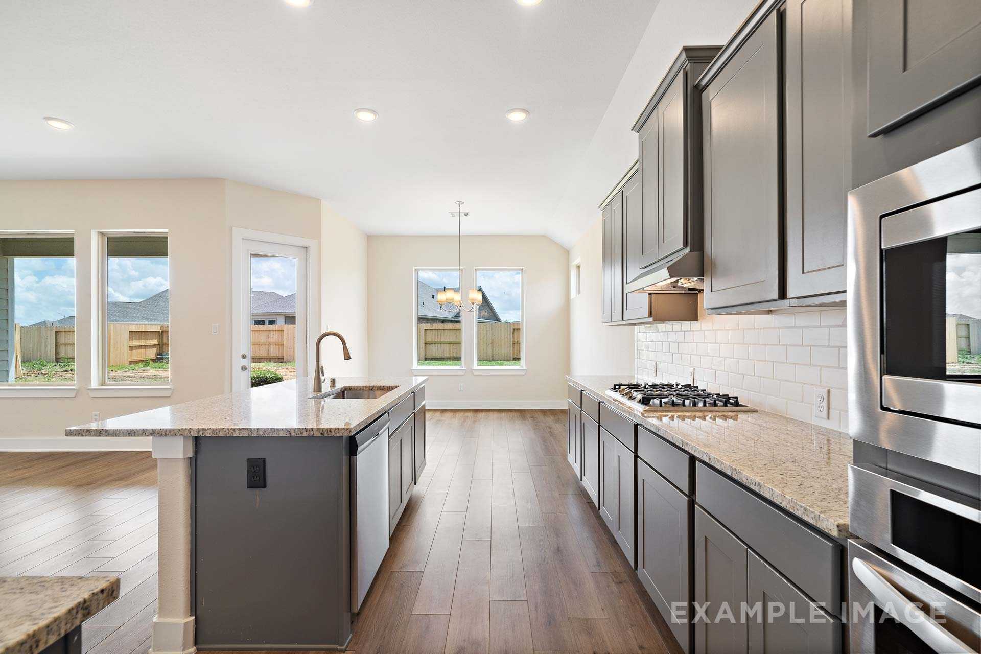 Modern open-concept kitchen in The Diana C with gray shaker cabinets, quartz island, stainless steel appliances, and hardwood floors