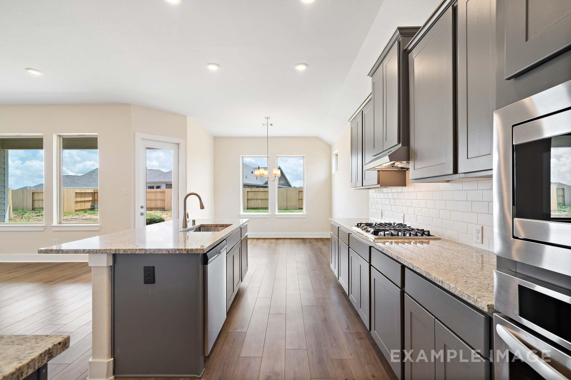 Modern open-concept kitchen in The Diana C with gray shaker cabinets, quartz island, stainless steel appliances, and hardwood floors