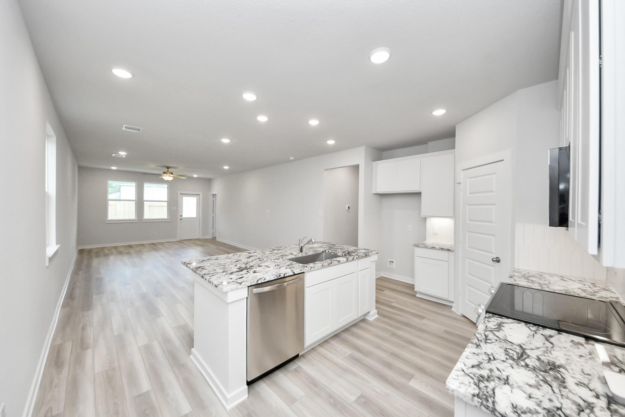 Modern open-concept kitchen with granite island and white cabinetry in The Sabine F floor plan, Liberty Estates, Texas.