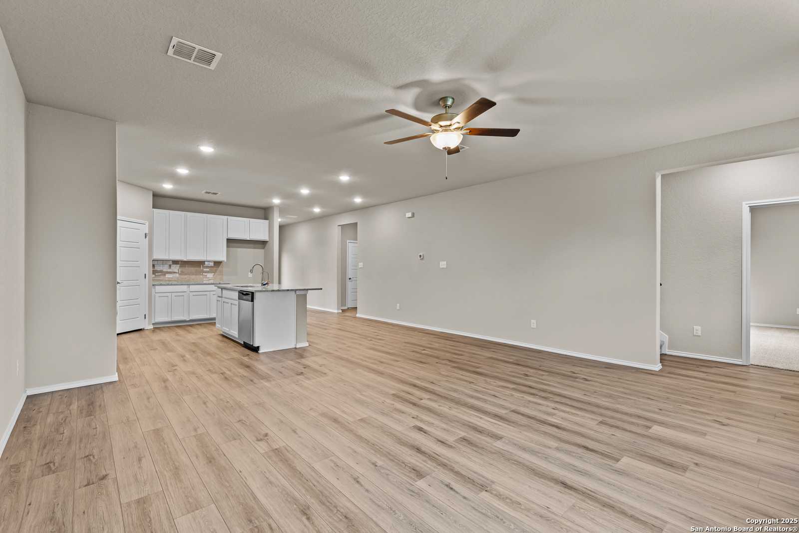 Spacious open kitchen with white cabinets, large island, and hardwood floors in Davidson Homes The Douglas F, San Antonio