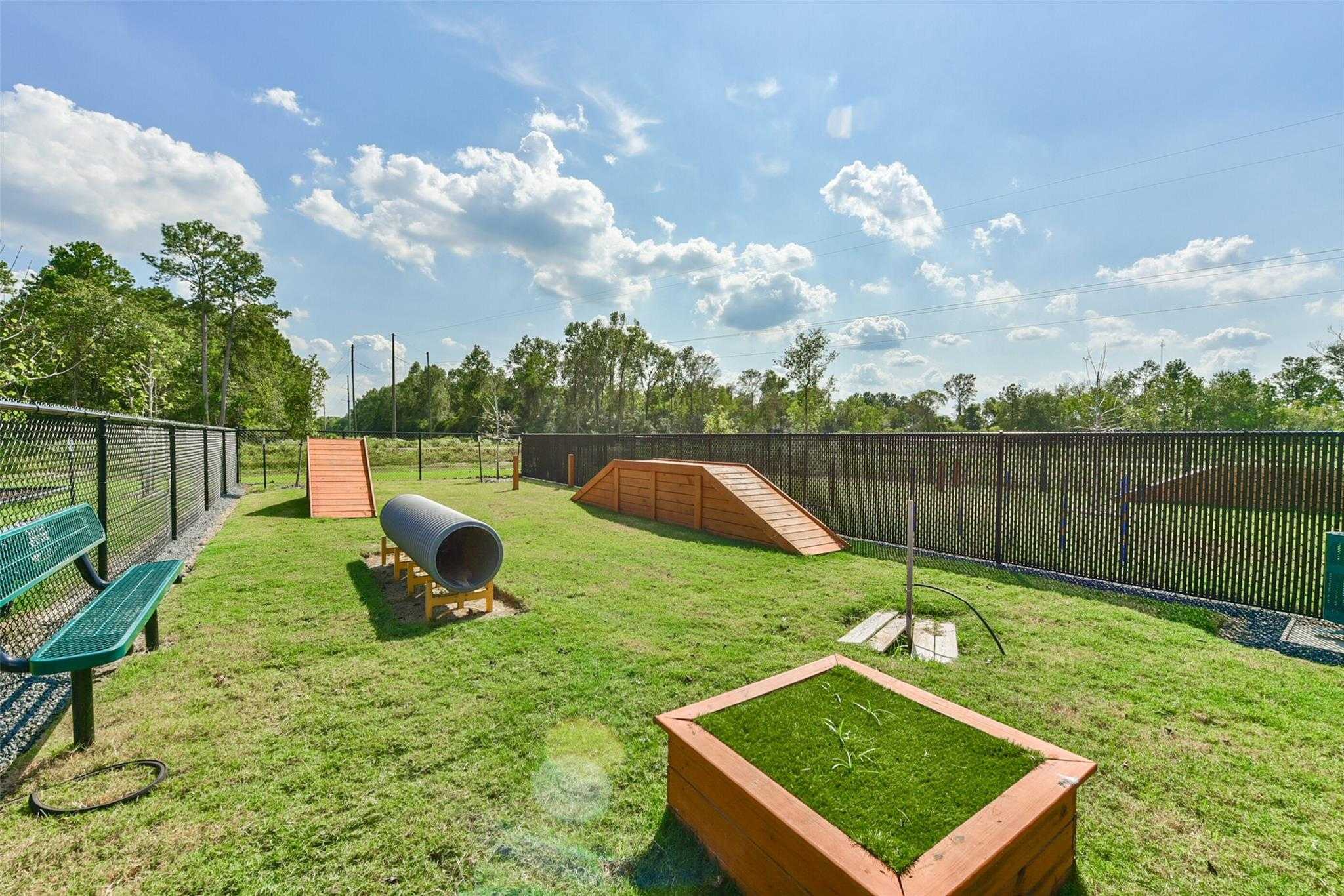 Fenced dog park with agility ramps, tunnel, benches, and turf in The Villages at WestPointe, Dayton, Texas
