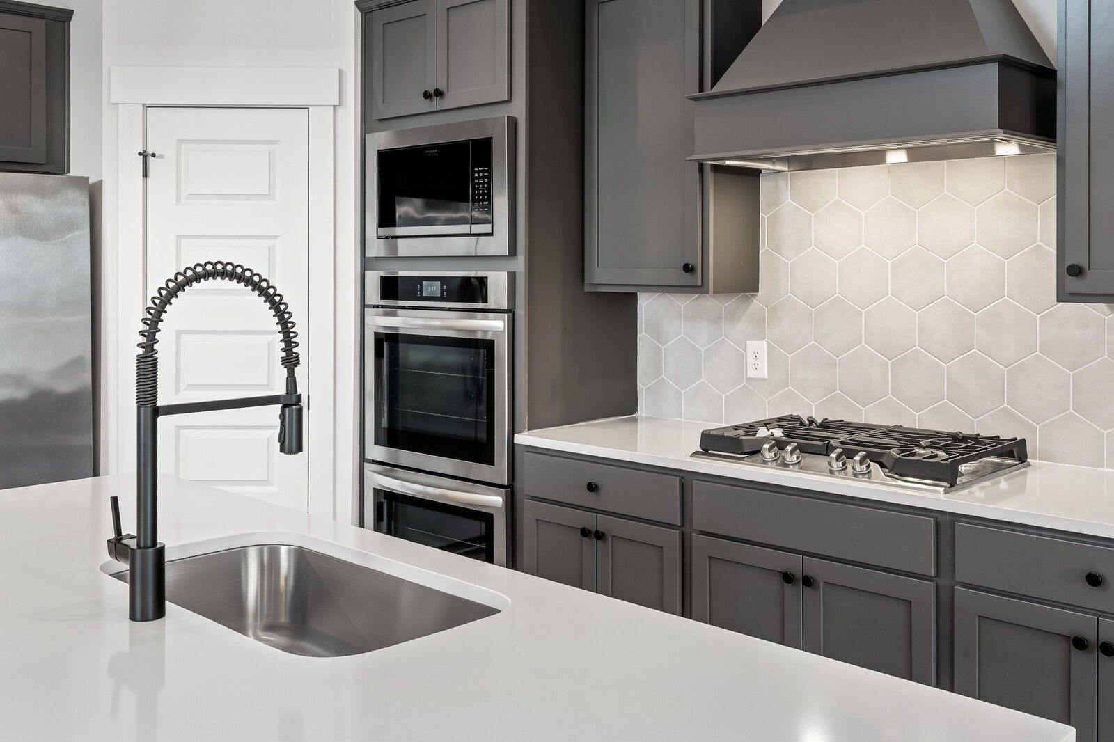 Modern kitchen featuring gray shaker cabinets, white quartz counters, stainless steel double oven and gas cooktop in Davidson Homes The Ridgeport, Gallatin, TN