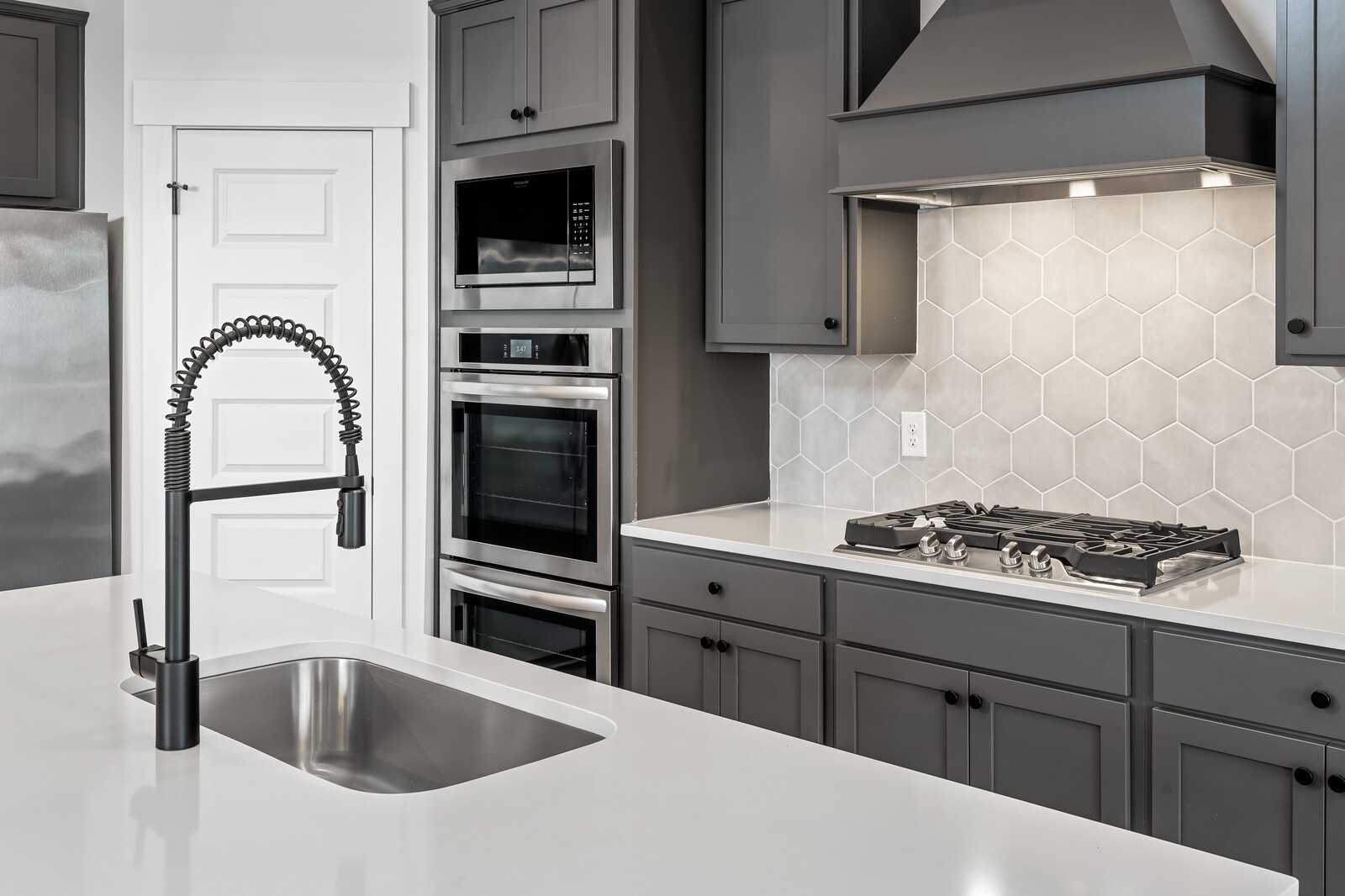 Modern kitchen featuring gray shaker cabinets, white quartz counters, stainless steel double oven and gas cooktop in Davidson Homes The Ridgeport, Gallatin, TN