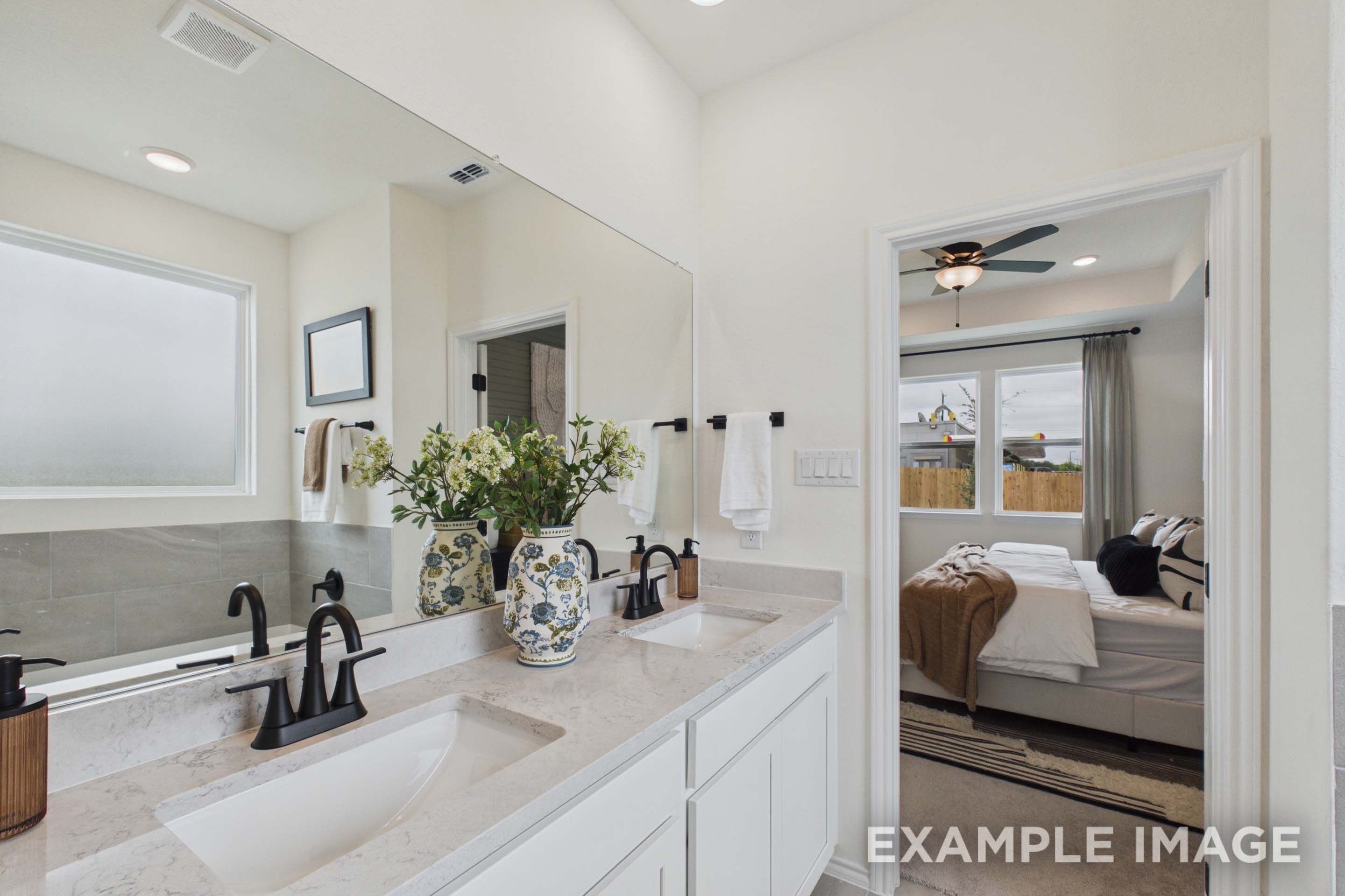Master suite bathroom in The Laurel G featuring a dual-sink vanity, quartz countertops, and view into the bedroom.